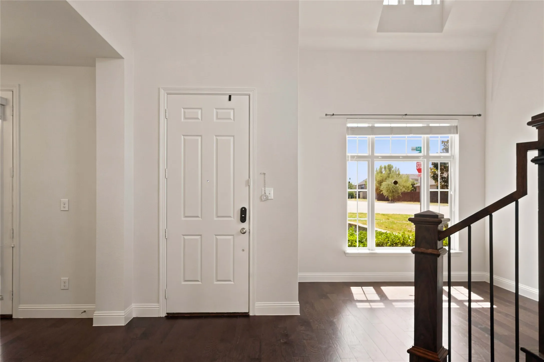 Dark wood-finish flooring with white baseboards, a paneled front entry door, and a white framed window with multiple panes