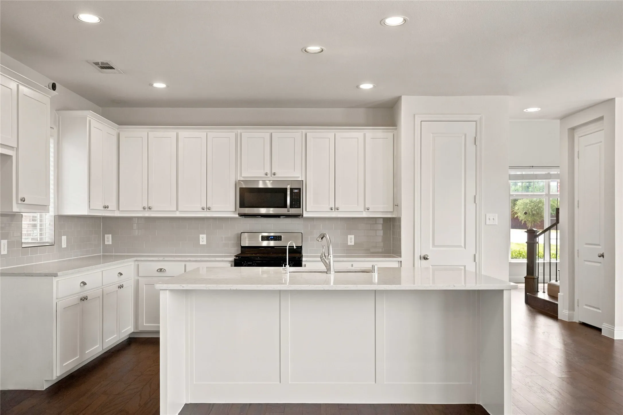 Kitchen featuring white shaker cabinetry, stainless steel appliances, light-toned countertops, and wood-finish flooring