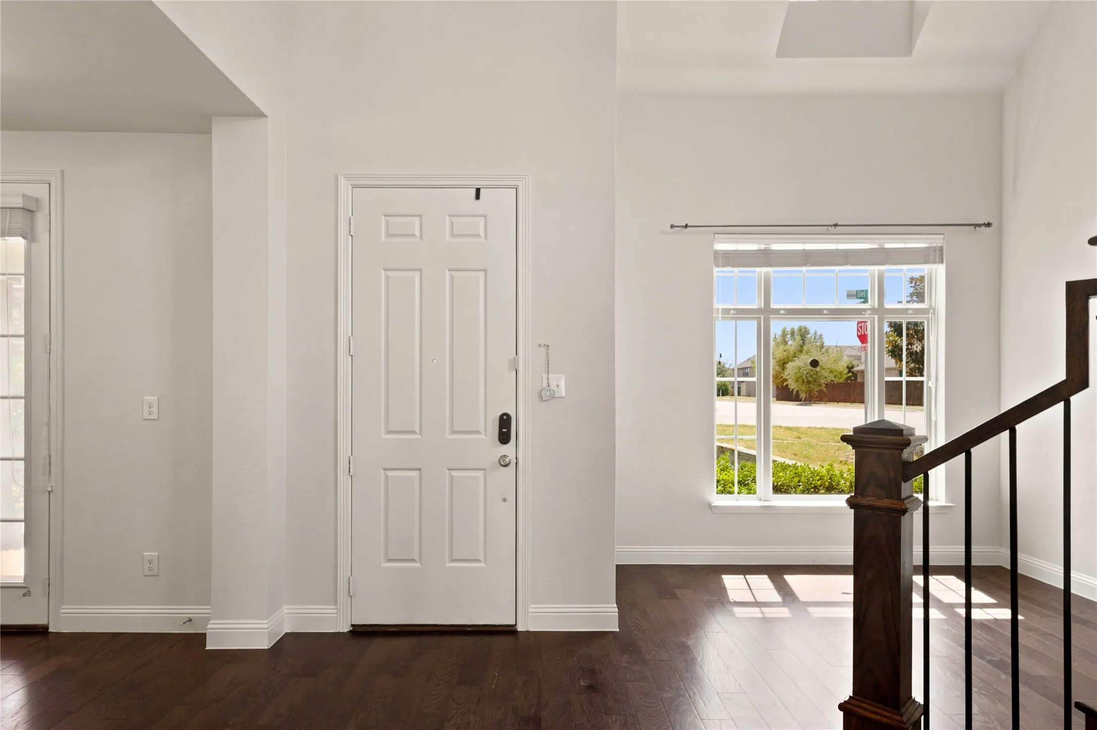 Dark wood-finish flooring, white paneled entry door, transom window, and a wood newel post with black metal balusters