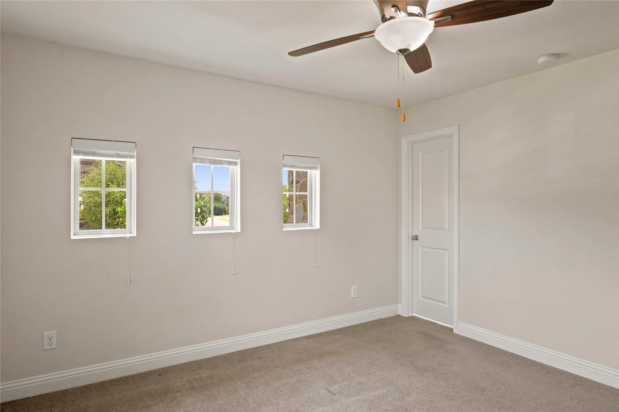Carpeted flooring, three transom windows, a ceiling fan with integrated lighting, and a white paneled door
