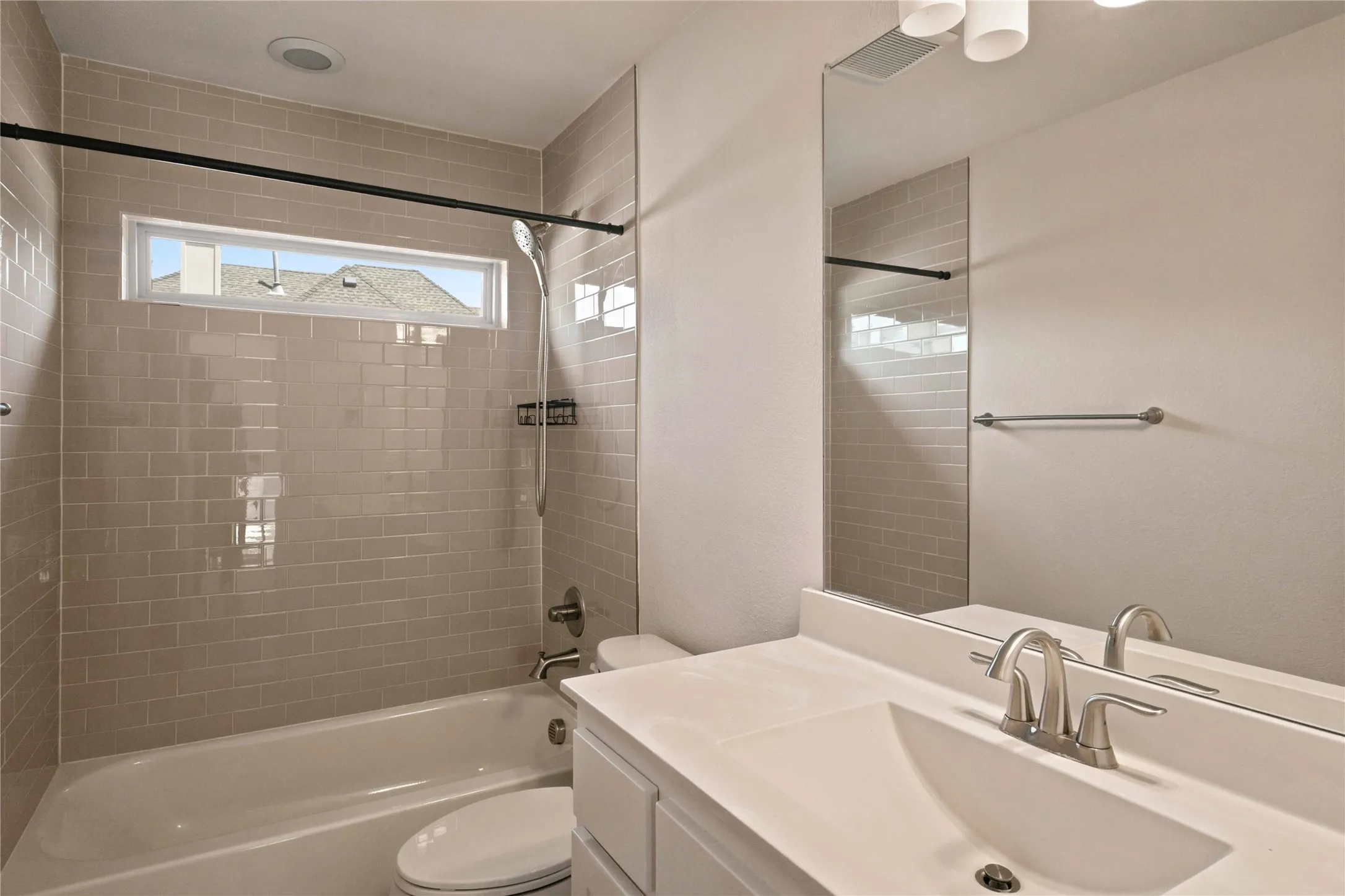 Integrated shower and tub with subway tile surround, sleek vanity with single basin sink, and a long horizontal window
