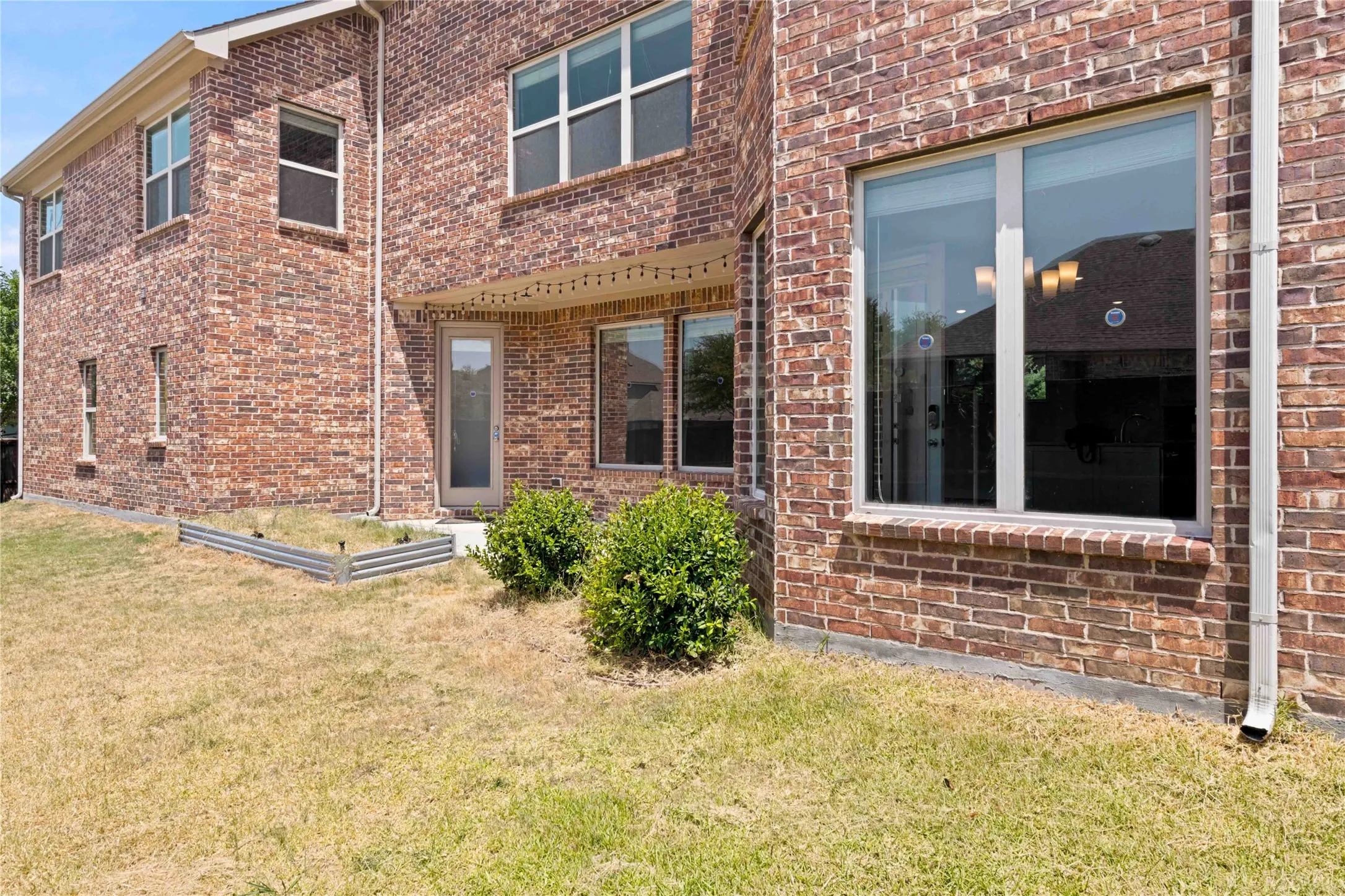 Brick exterior with multiple windows, downspout, and a raised garden bed