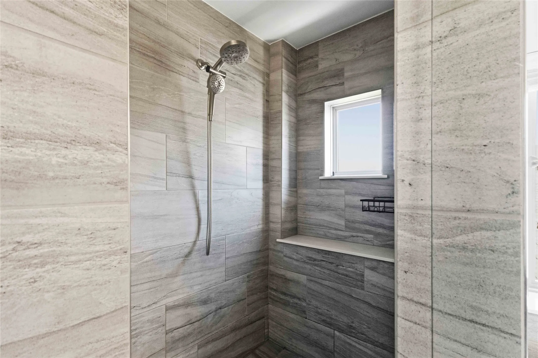 Shower enclosure with floor-to-ceiling tile, a built-in bench, a window, and a wall-mounted showerhead