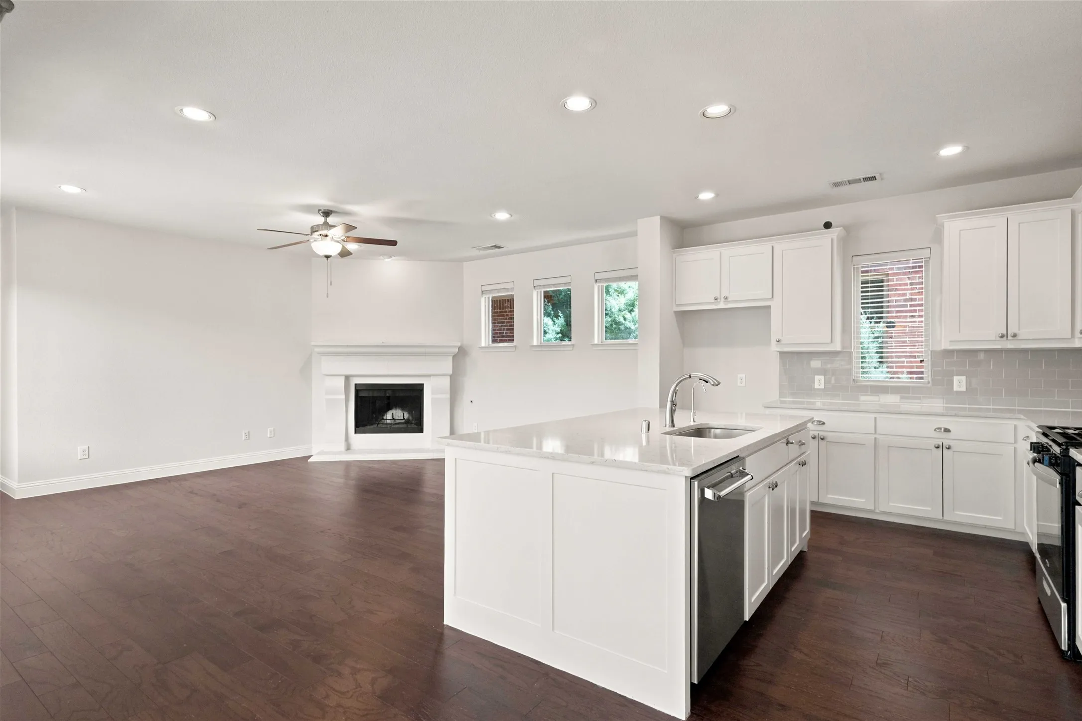 Wood-finish flooring, recessed lighting, white kitchen cabinetry, a center island with a sink, and a fireplace with a mantel