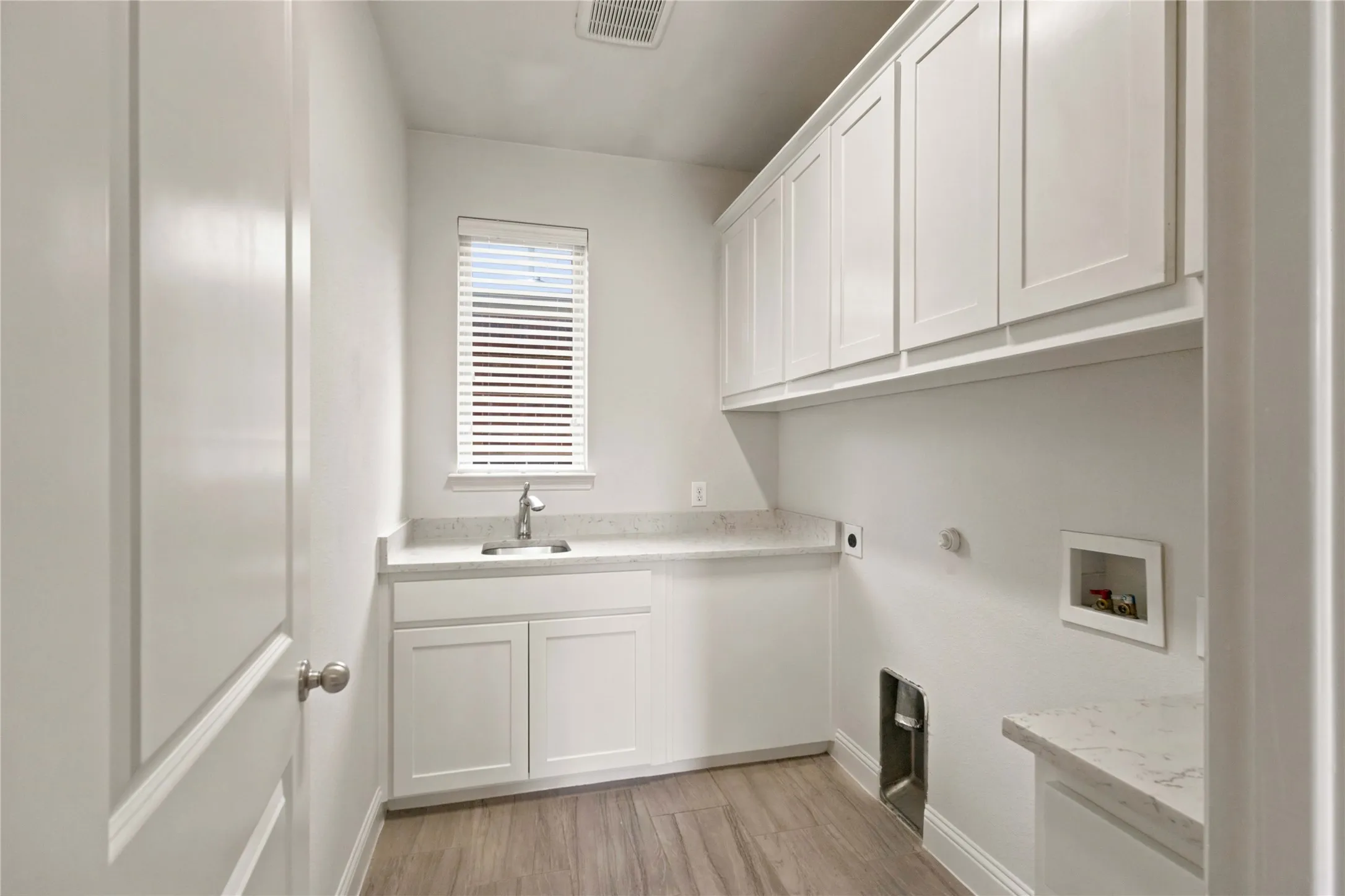 White shaker-style cabinetry with upper storage, light-toned countertop, stainless steel sink with faucet, and wood-finish flooring