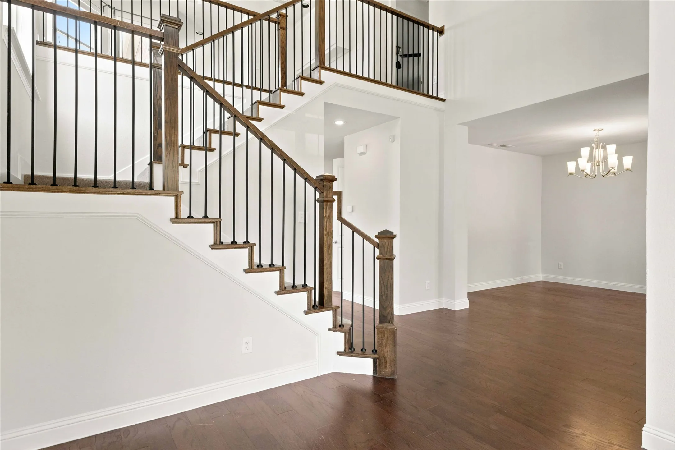 Two-story foyer with hardwood flooring, a staircase featuring wood treads and wrought iron balusters, and a second-story landing overlooking the space