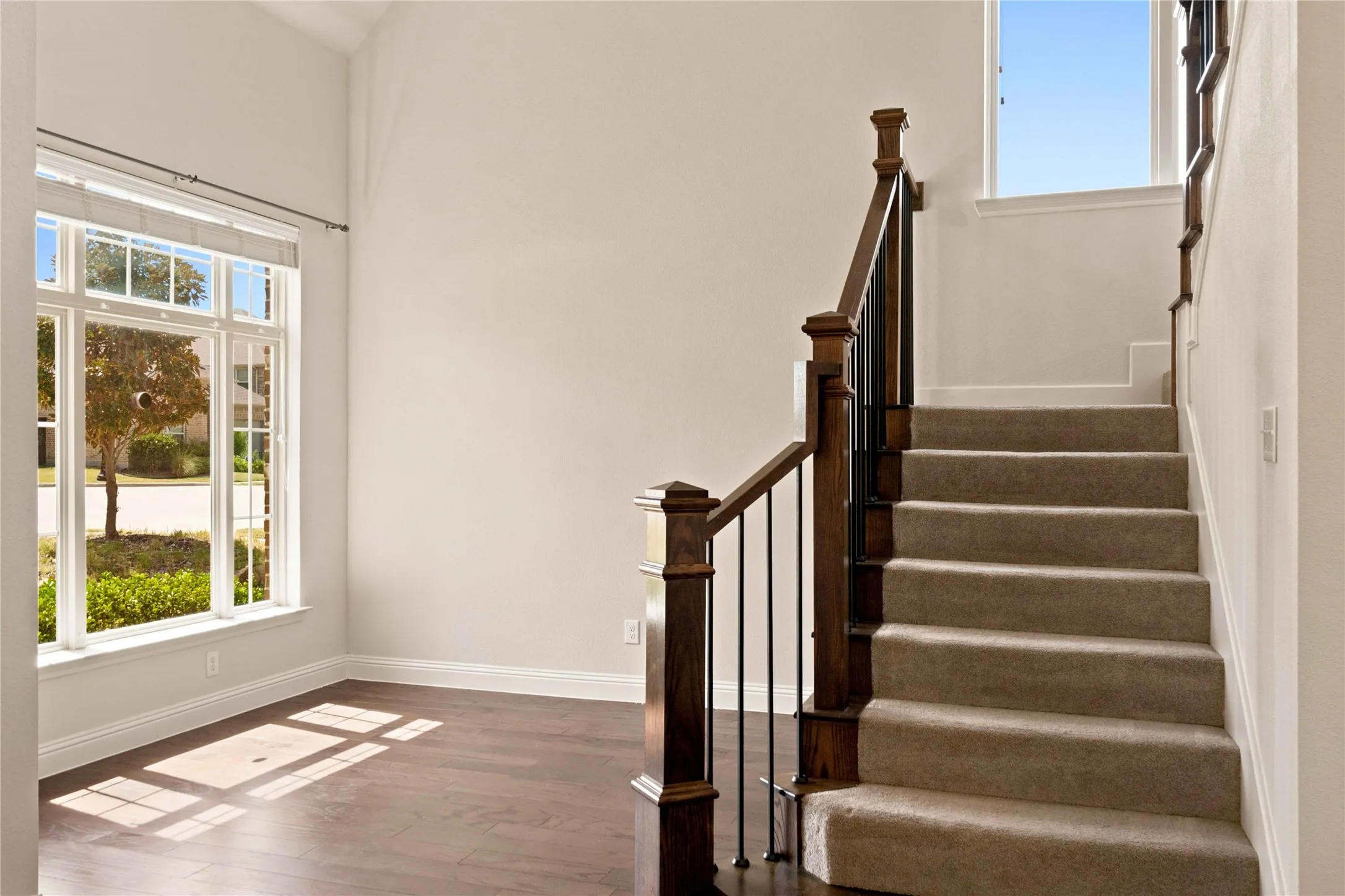 Vaulted ceiling with an expansive window, rich wood-finish flooring, and a staircase featuring a wood newel post with metal balusters