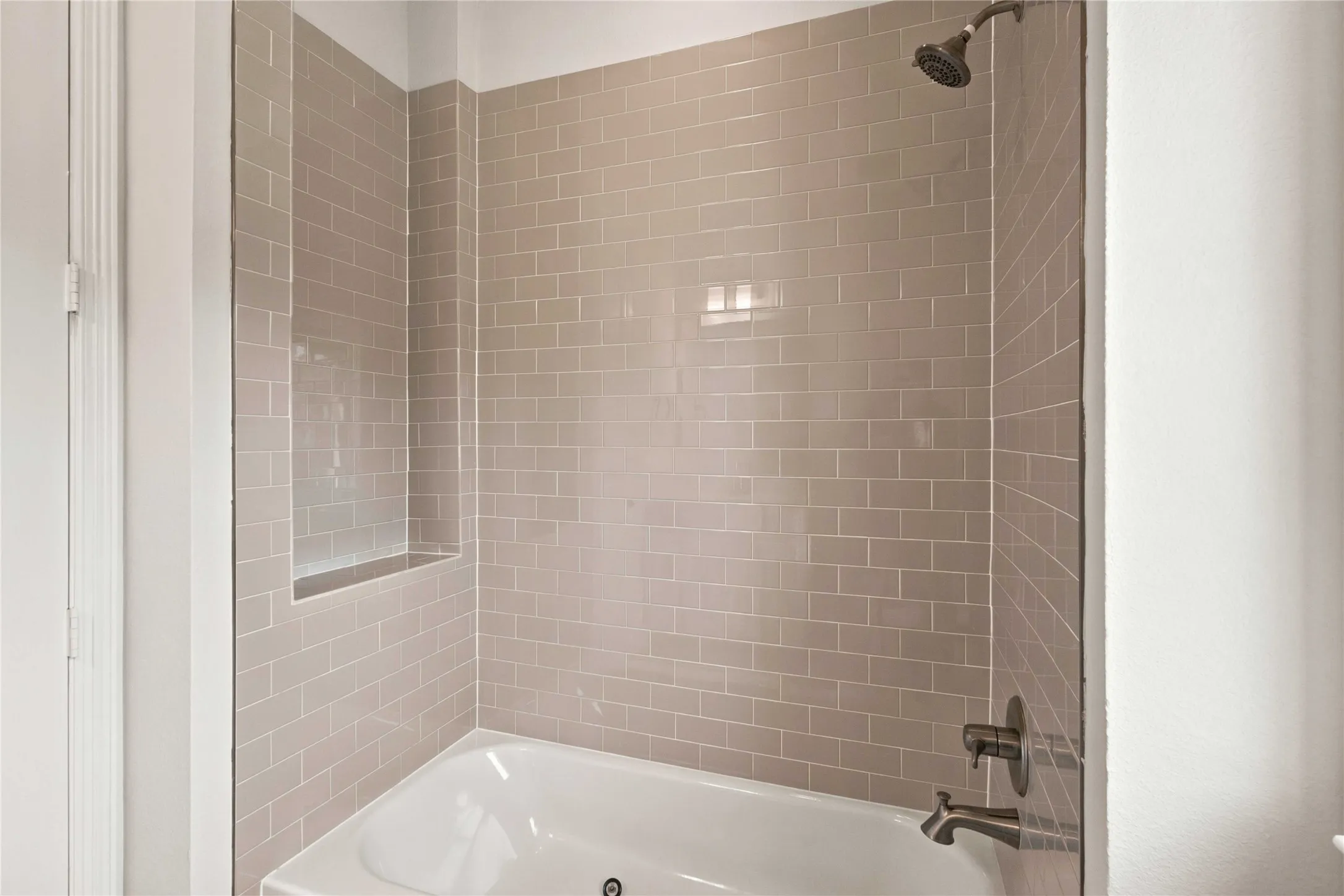 White soaking tub with subway tile surround, integrated shower niche, bronze-finish shower head, and matching bronze-finish tub filler