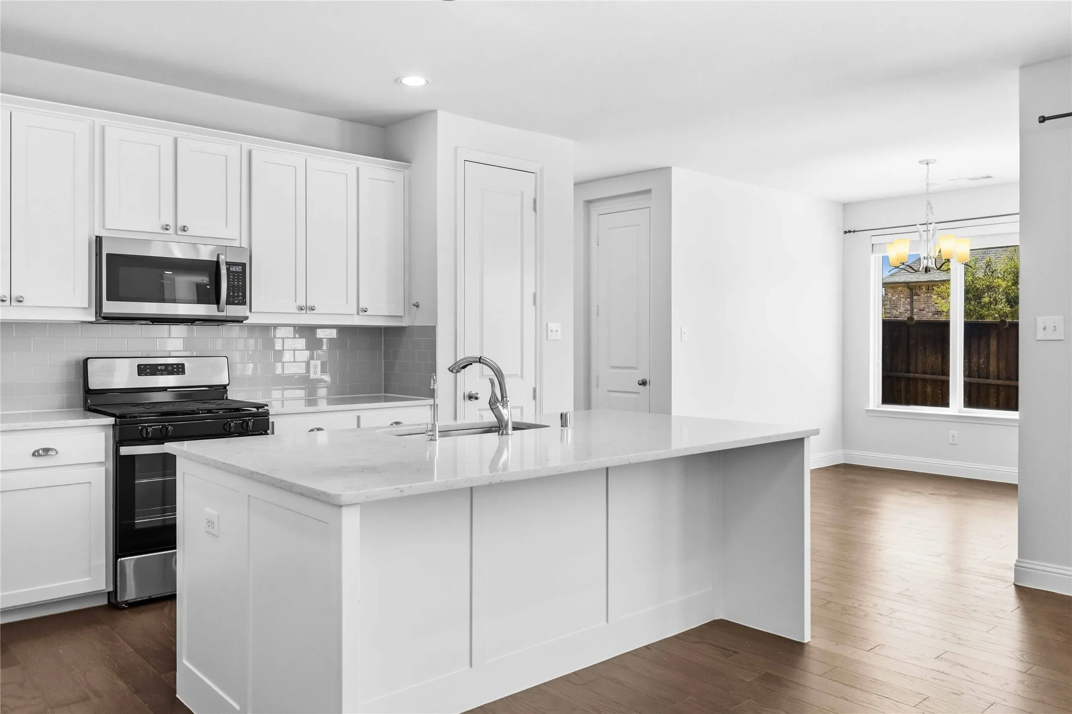 Kitchen featuring white shaker-style cabinetry, stainless steel appliances, a center island with a sink, and wood-finish flooring