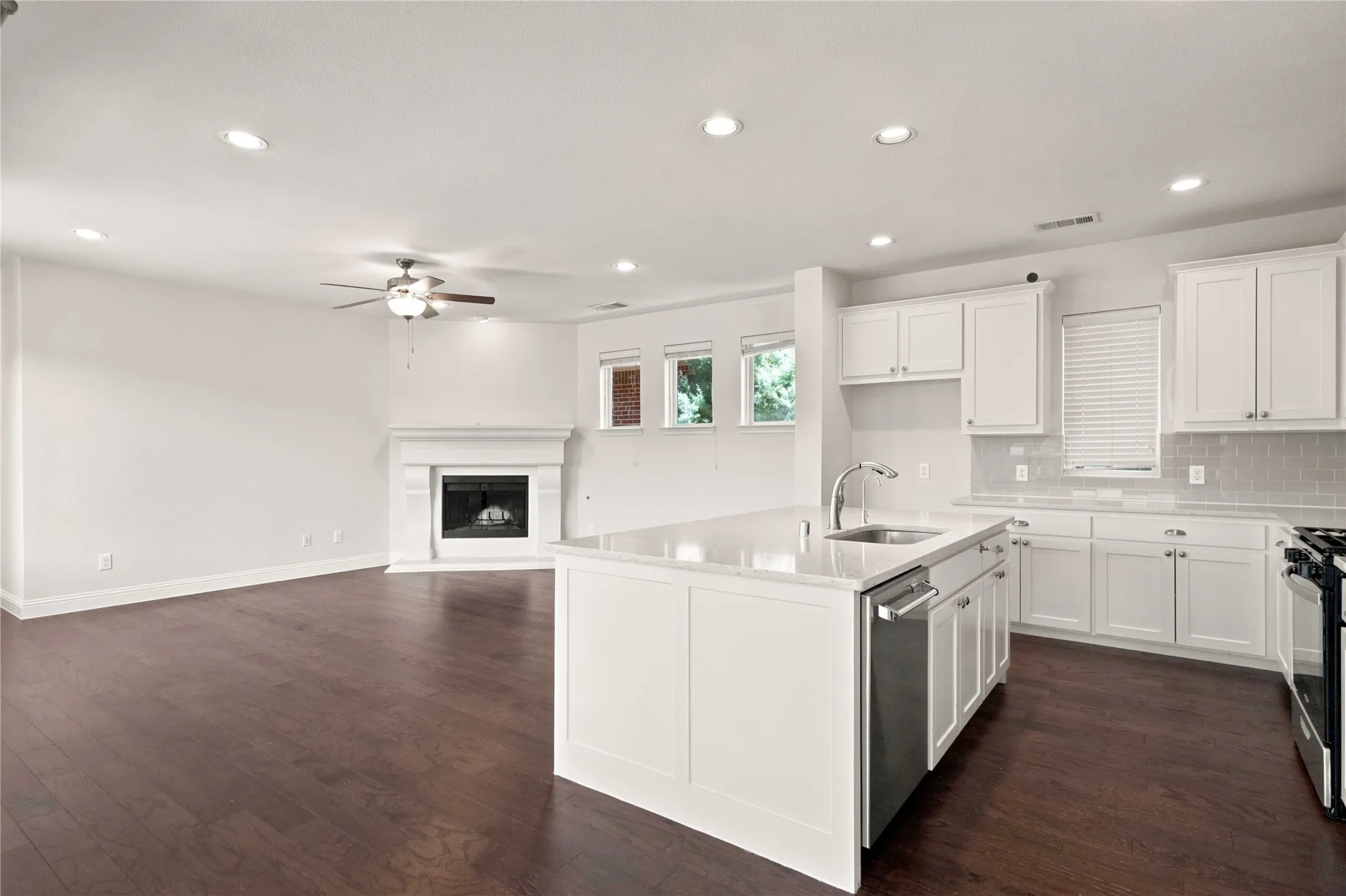 Open-concept living area with dark wood-finish flooring, recessed lighting, and a white mantel fireplace