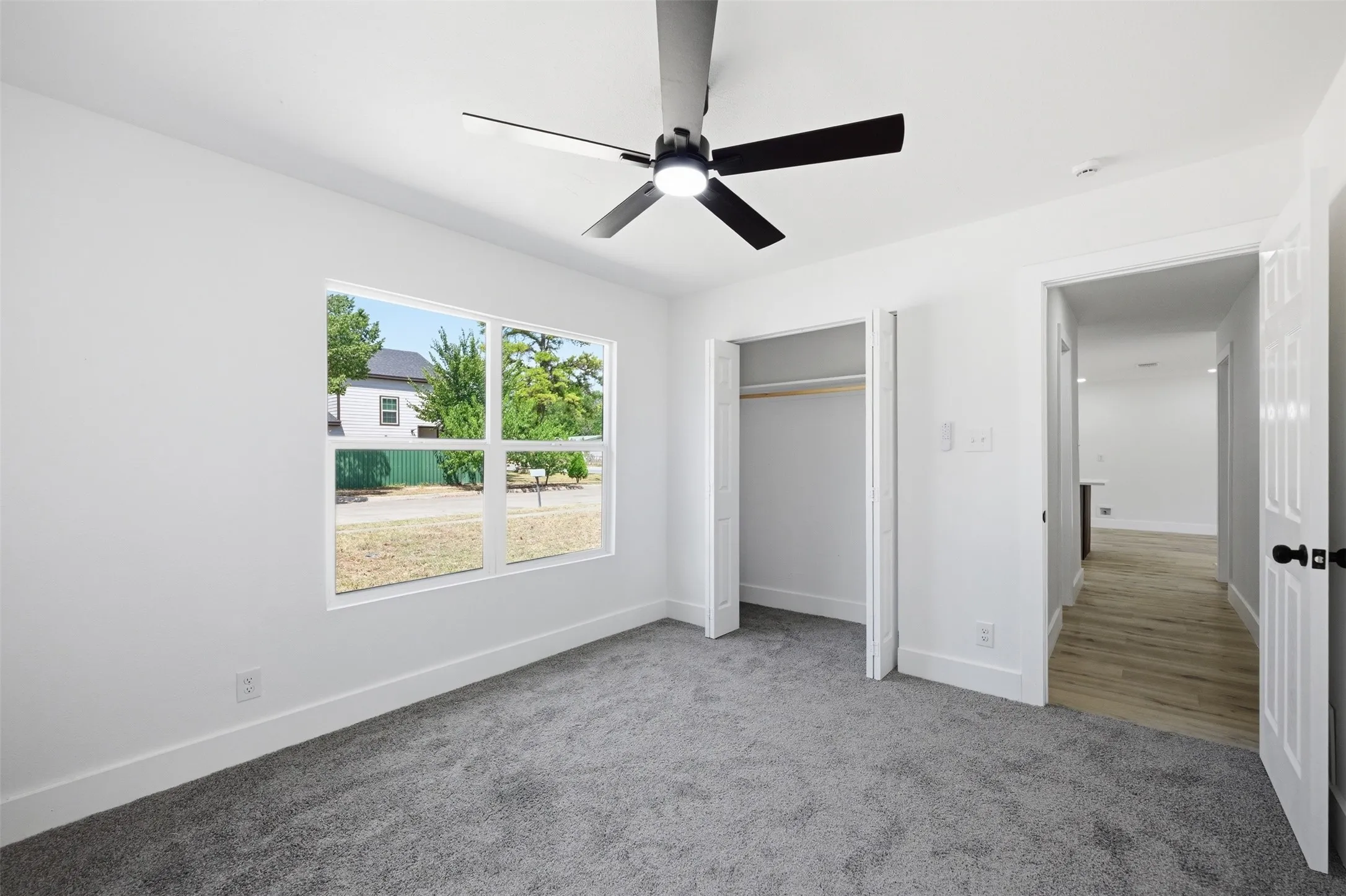 White walls with gray carpet flooring, a multi-pane window, a ceiling fan with integrated lighting, and a bi-fold door closet