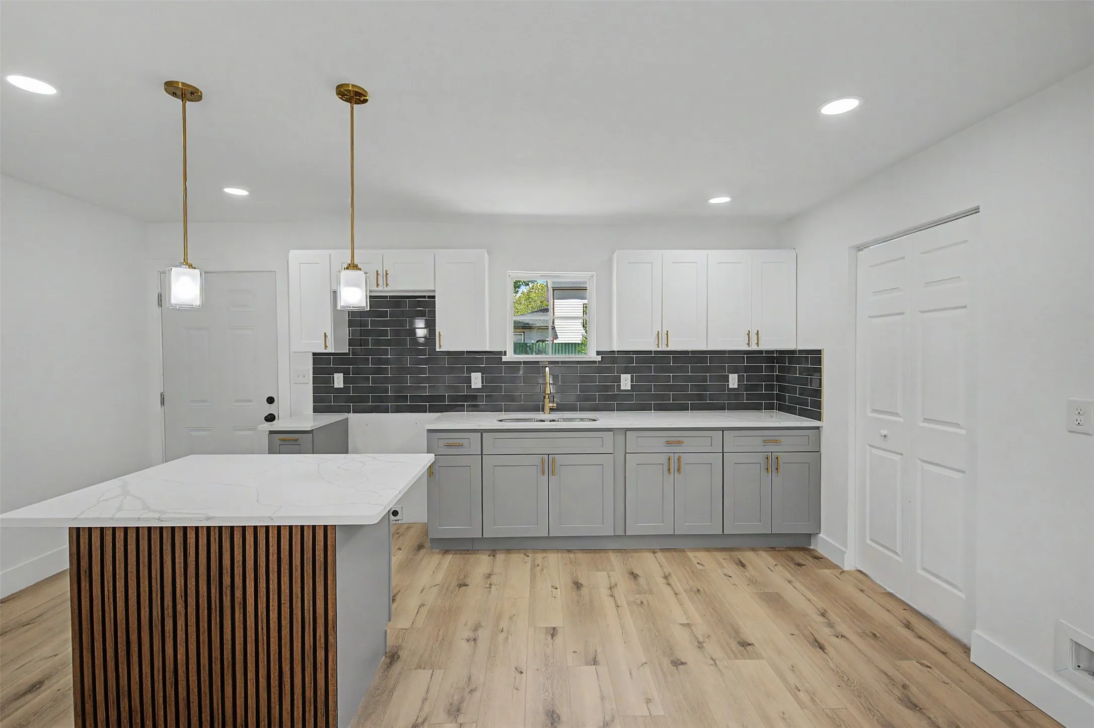 Modern kitchen featuring an island with a slatted wood-finish accent panel and white countertop, two-tone cabinetry, a dark subway tile backsplash, and wood-finish flooring