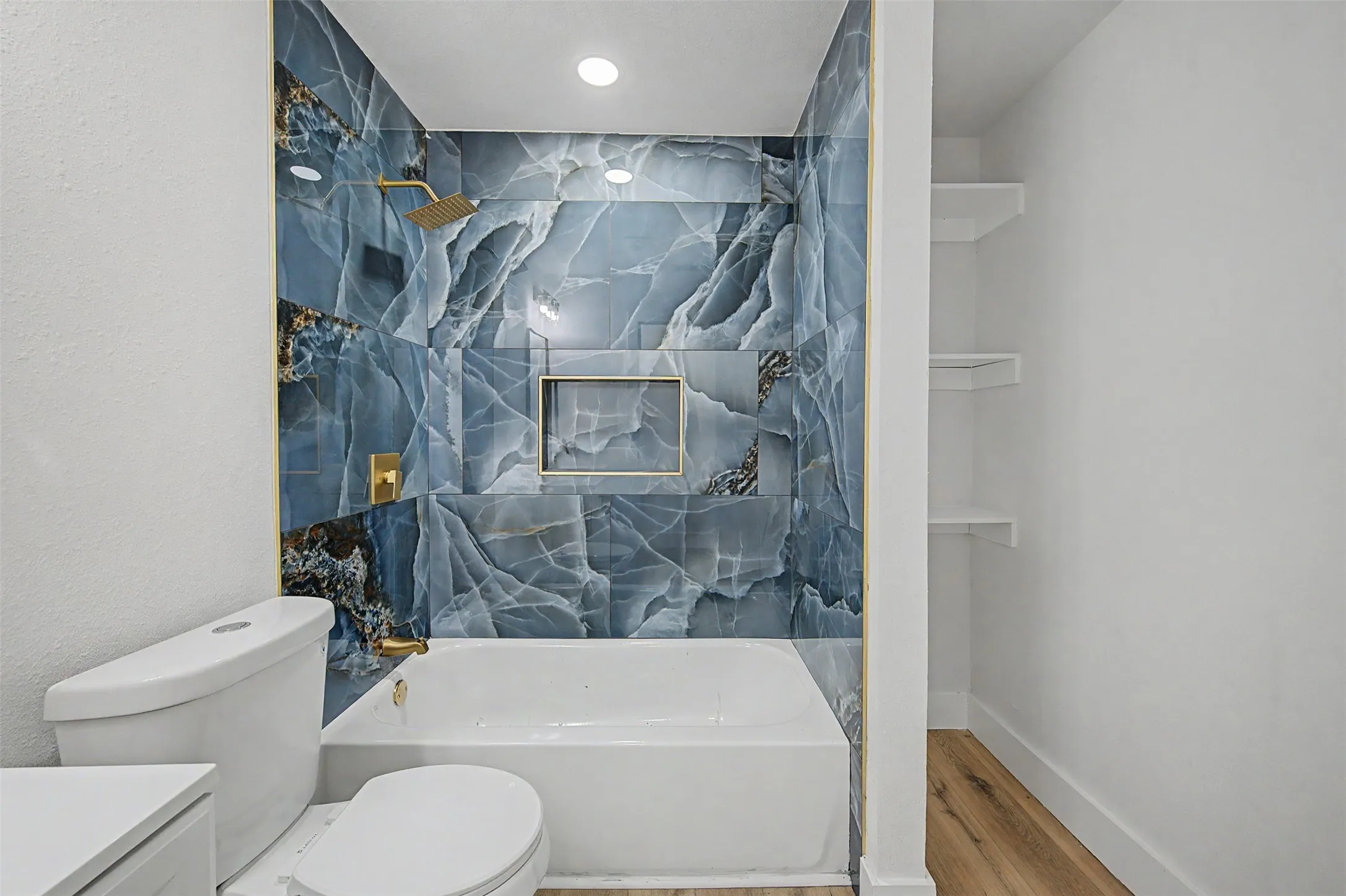 Bathtub with blue vein-cut tile surround, gold-finish fixtures, and a recessed shower niche