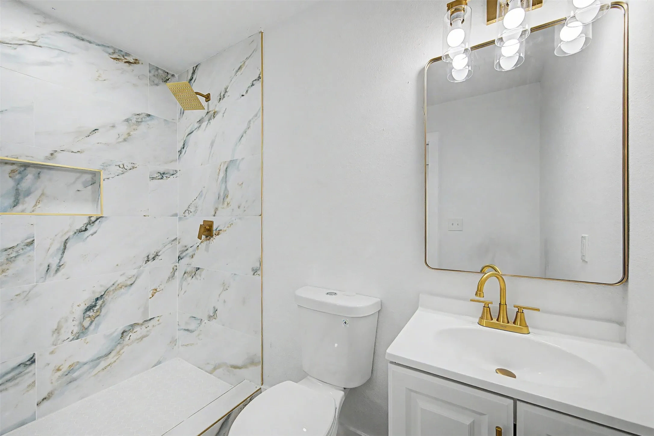 Tiled shower with a gold-finish rainfall showerhead, recessed shelf, and gold-finish trim