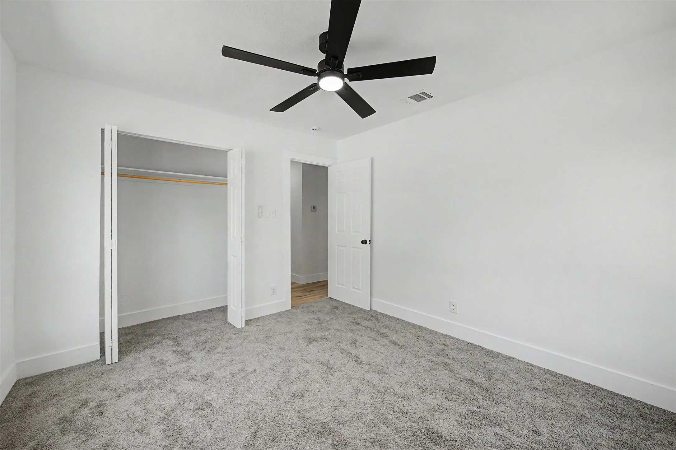 Plush gray carpet, bifold closet doors, and a black ceiling fan with integrated lighting
