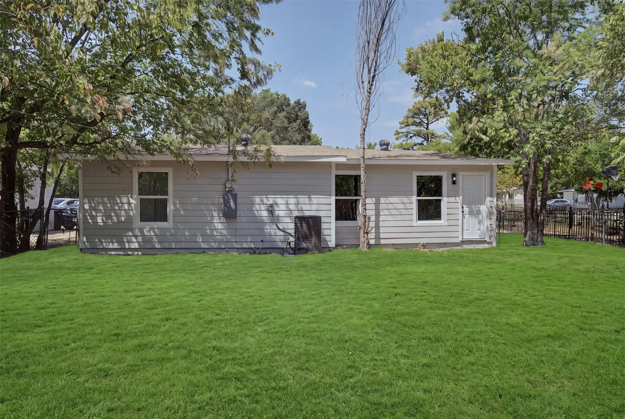 Expansive green lawn, light-colored siding, multiple windows, rear exterior door, partial fencing