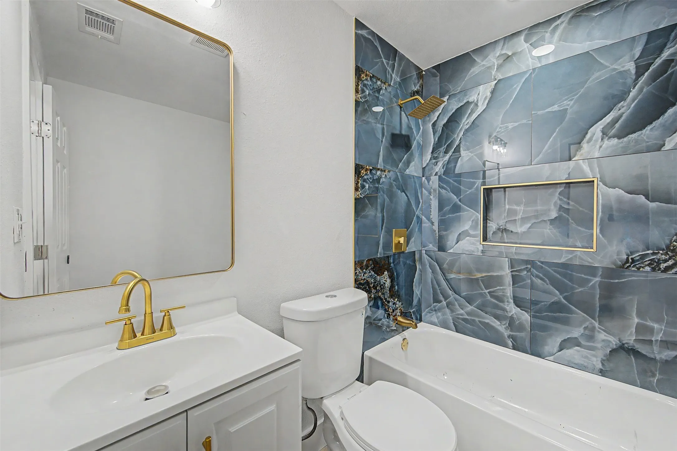 Modern bathroom featuring a white vanity with gold-finish hardware, a gold-framed mirror, and a toilet