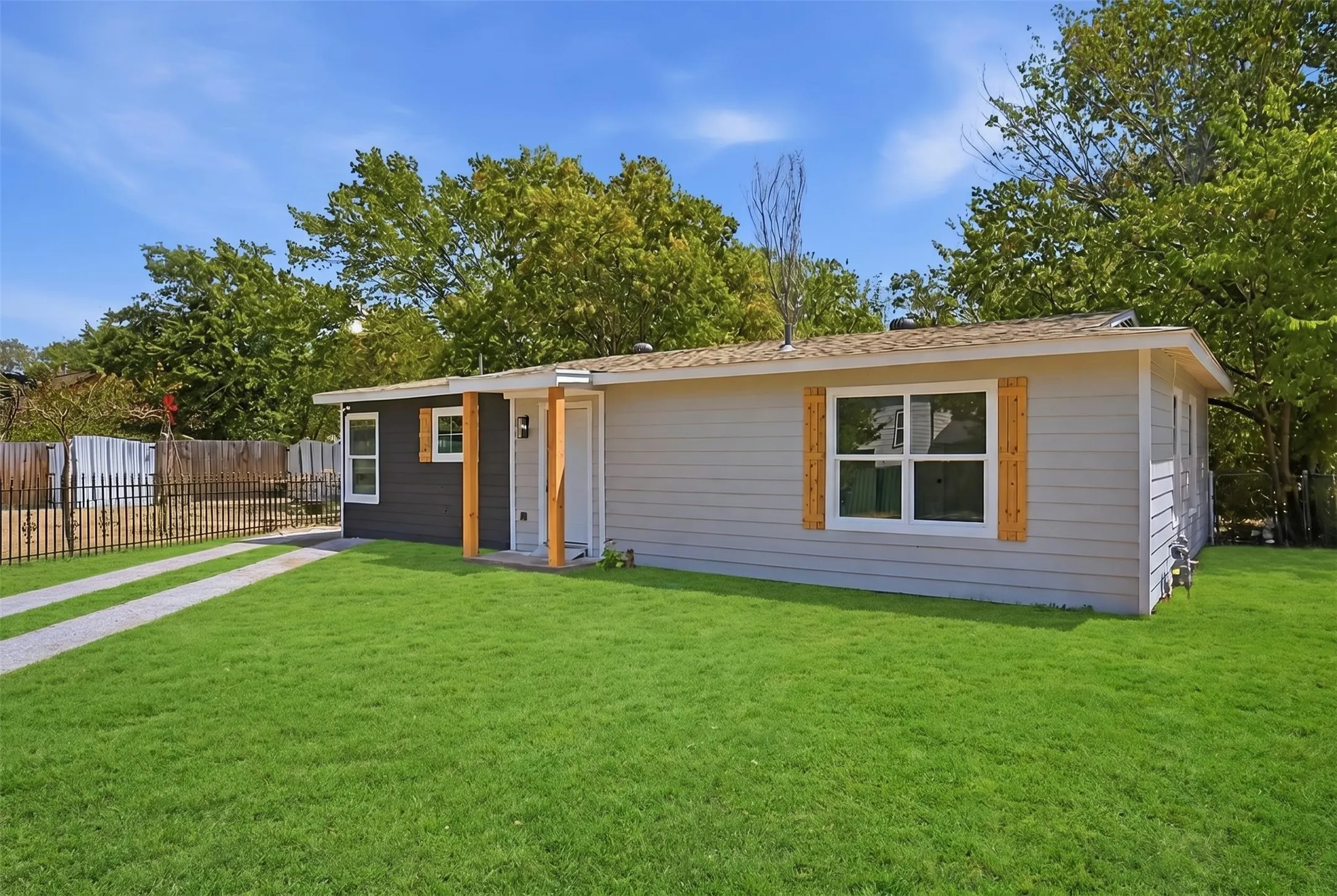 Contemporary exterior siding, wood-toned decorative shutters, white window frames, covered entry with wood-toned support beams, and a gravel driveway