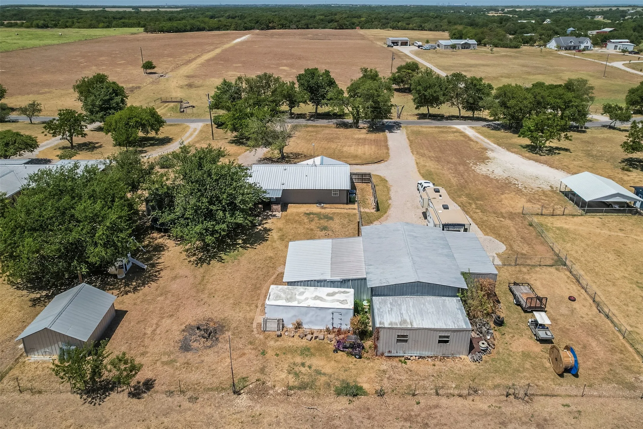 Expansive rural property featuring multiple outbuildings, mature trees, and gravel driveways