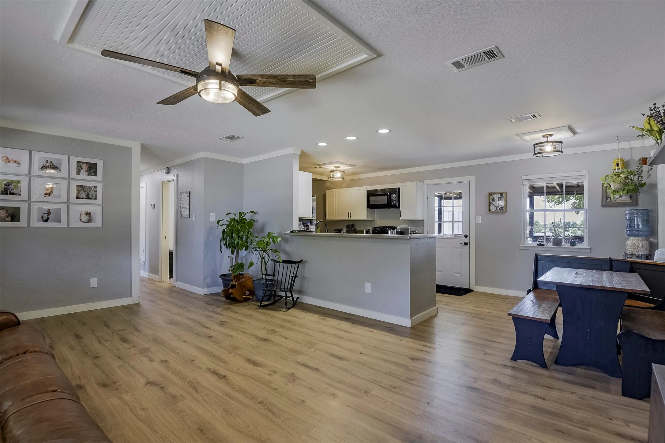 Wood-finish flooring throughout, tray ceiling with beadboard accent, recessed lighting, and kitchen with white cabinetry and black appliances