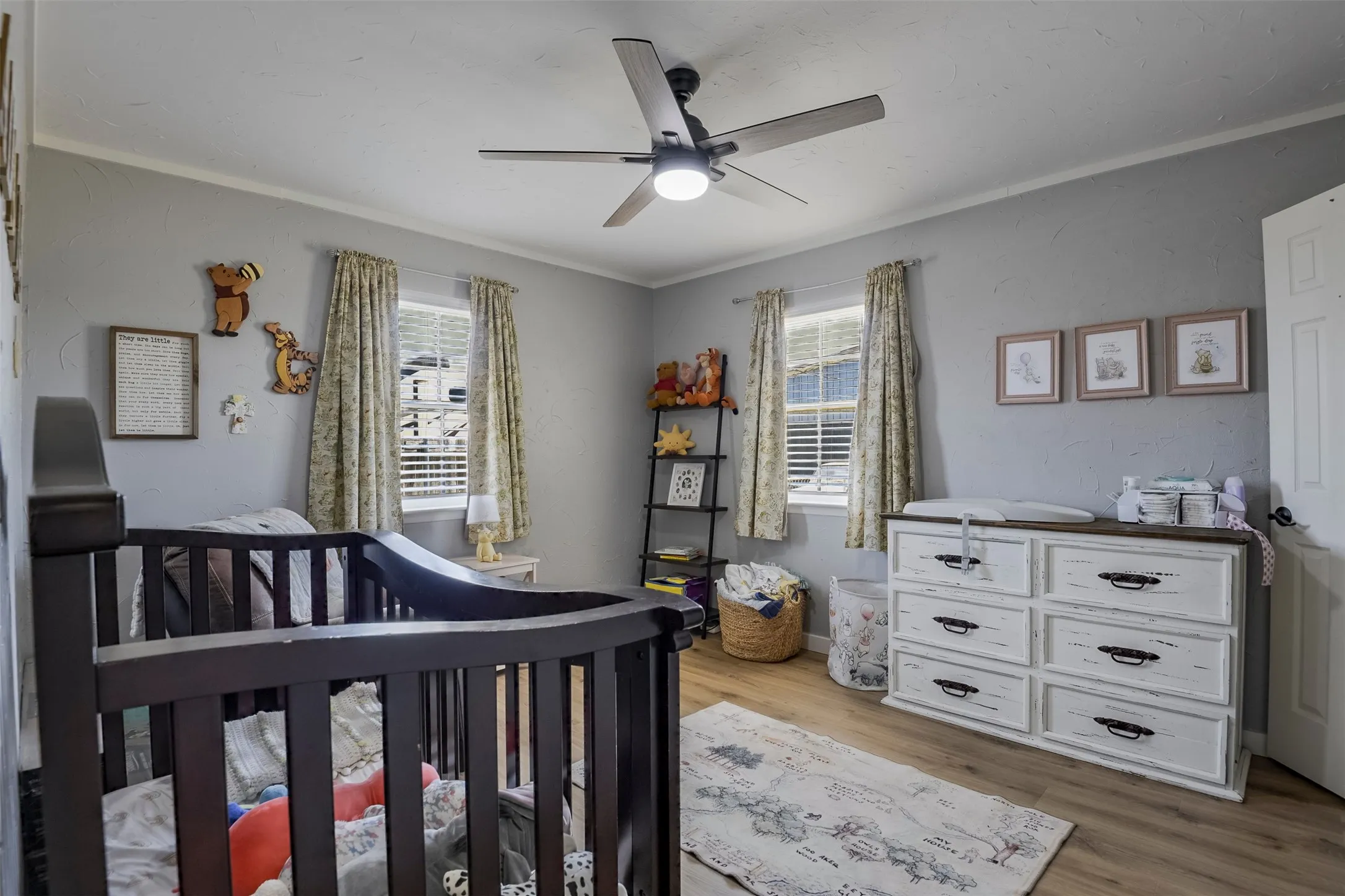 Crown molding, wood-finish flooring, two windows with blinds, a ceiling fan with integrated lighting, and a white paneled door