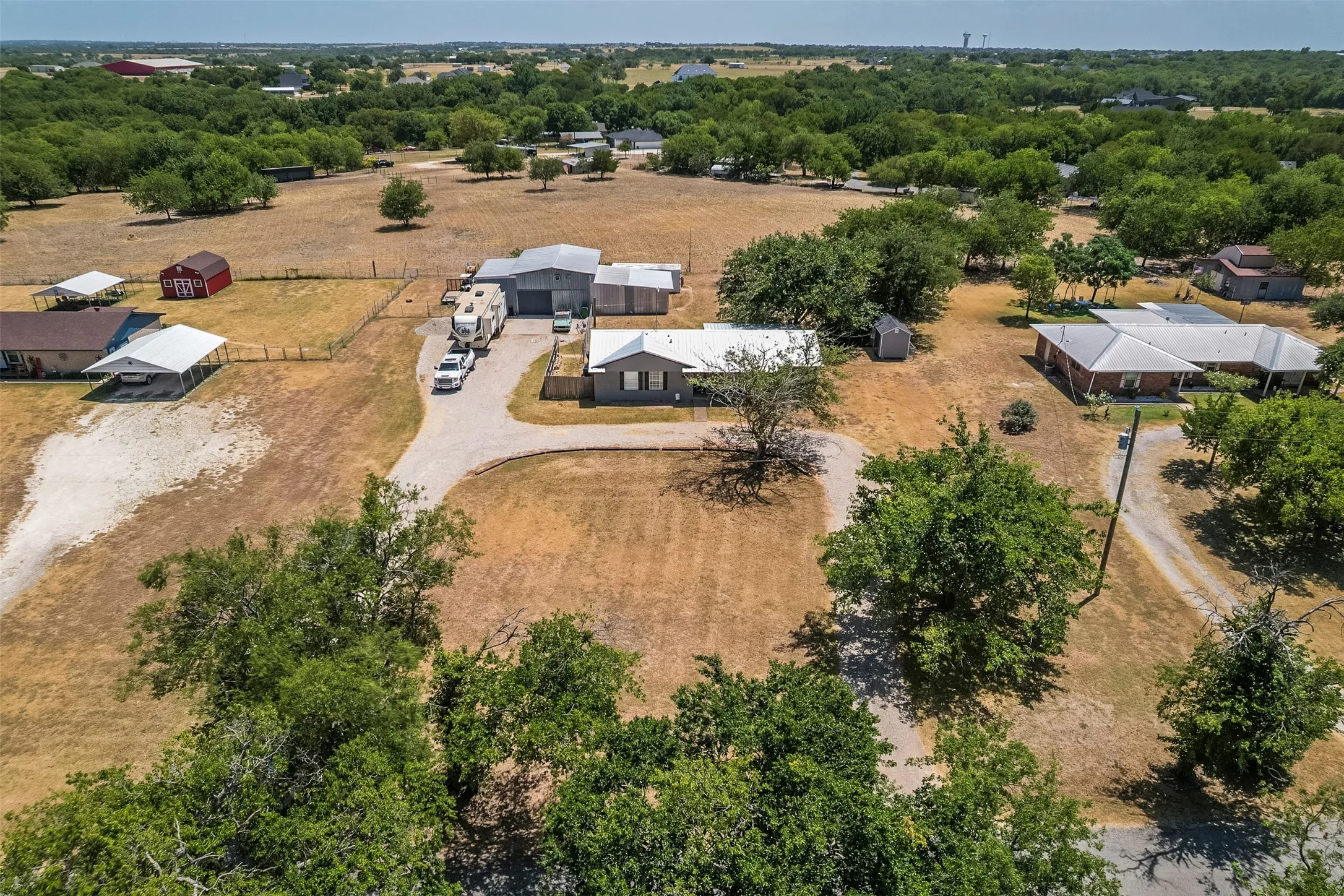 Expansive property featuring multiple structures, a gravel driveway, and mature trees throughout the landscape