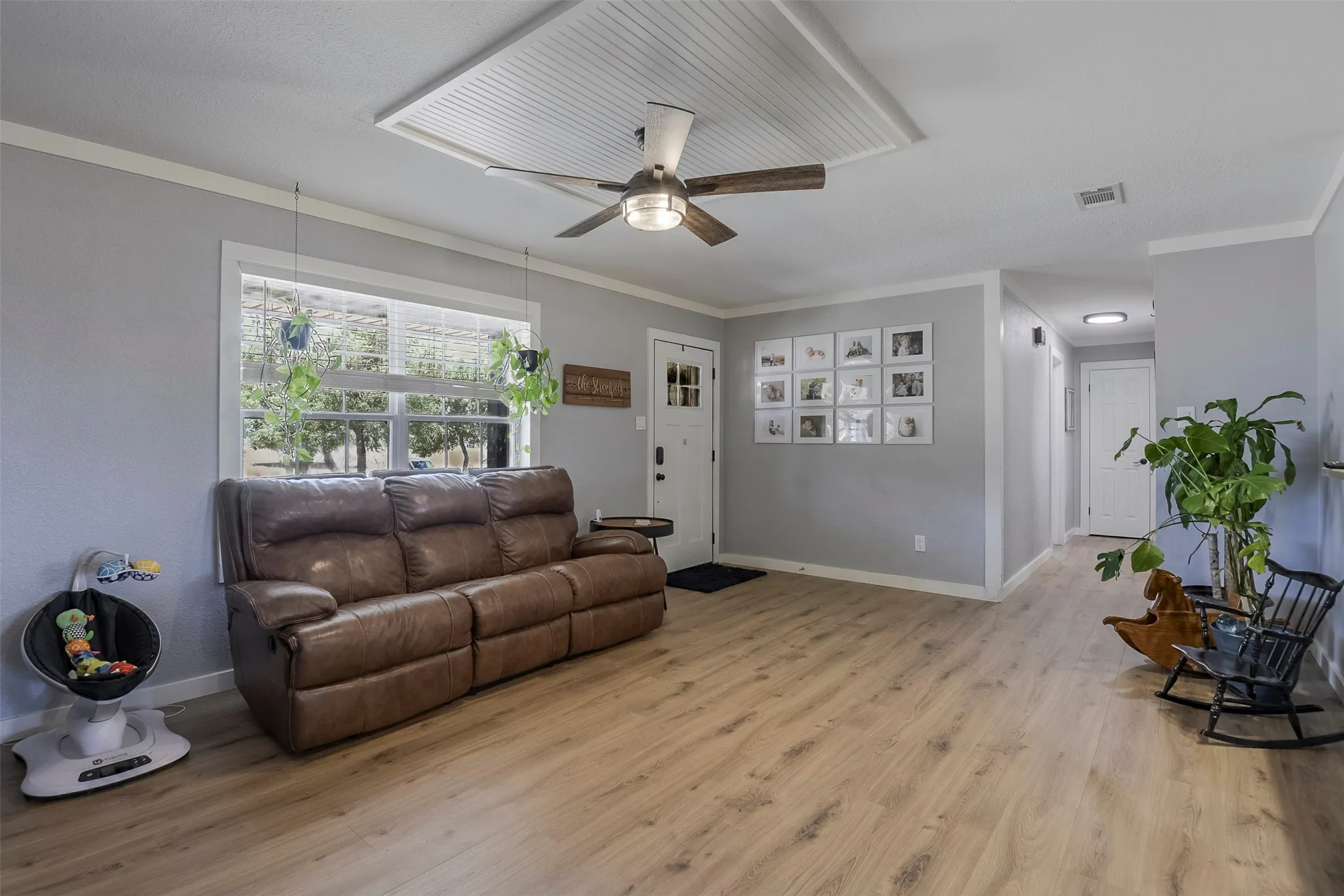 Spacious room featuring wood-finish flooring, light gray walls, a large window, and a ceiling fan with beadboard detailing