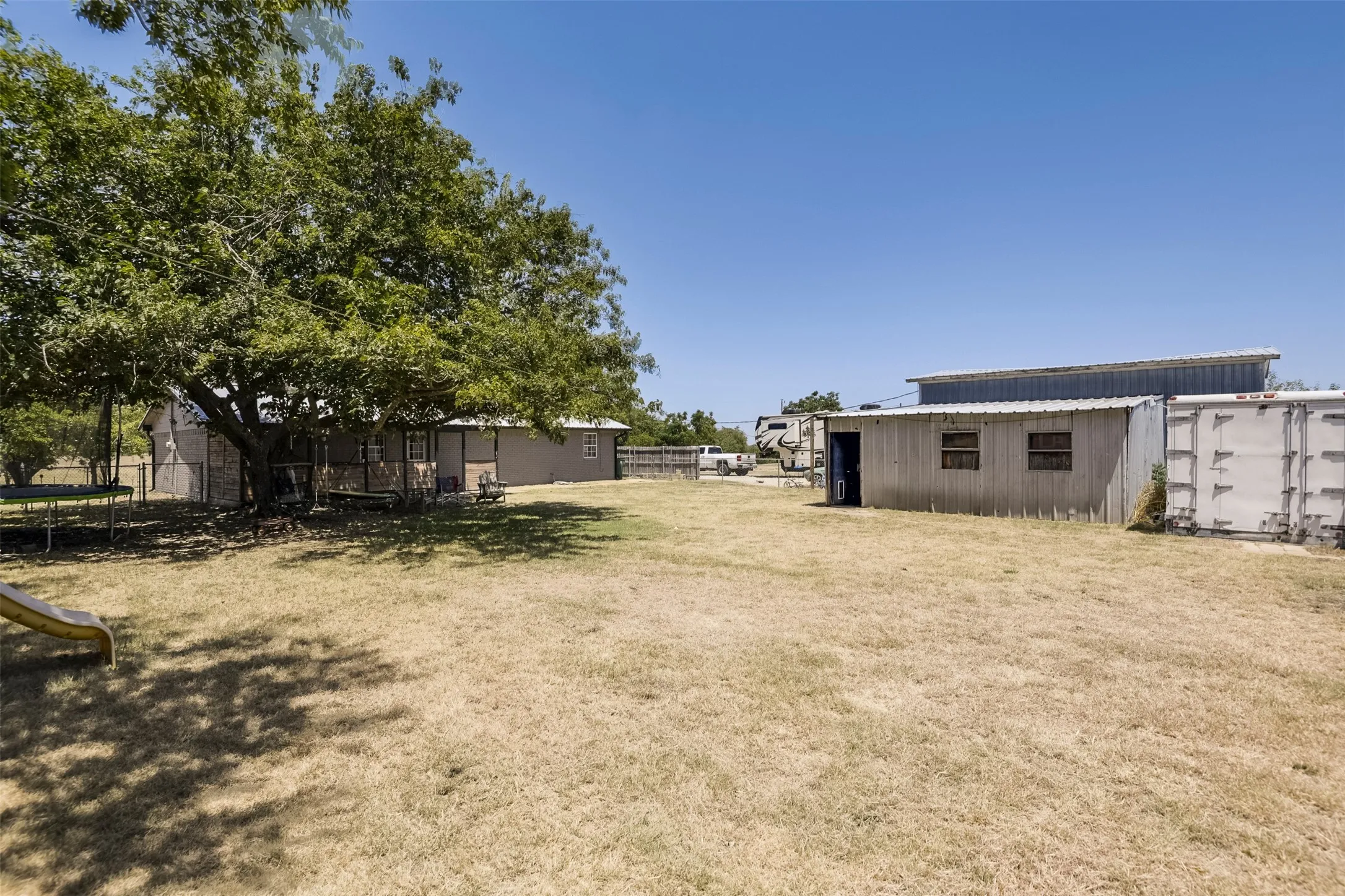Expansive yard featuring mature trees, a detached storage building with a metal roof, and an additional corrugated metal structure