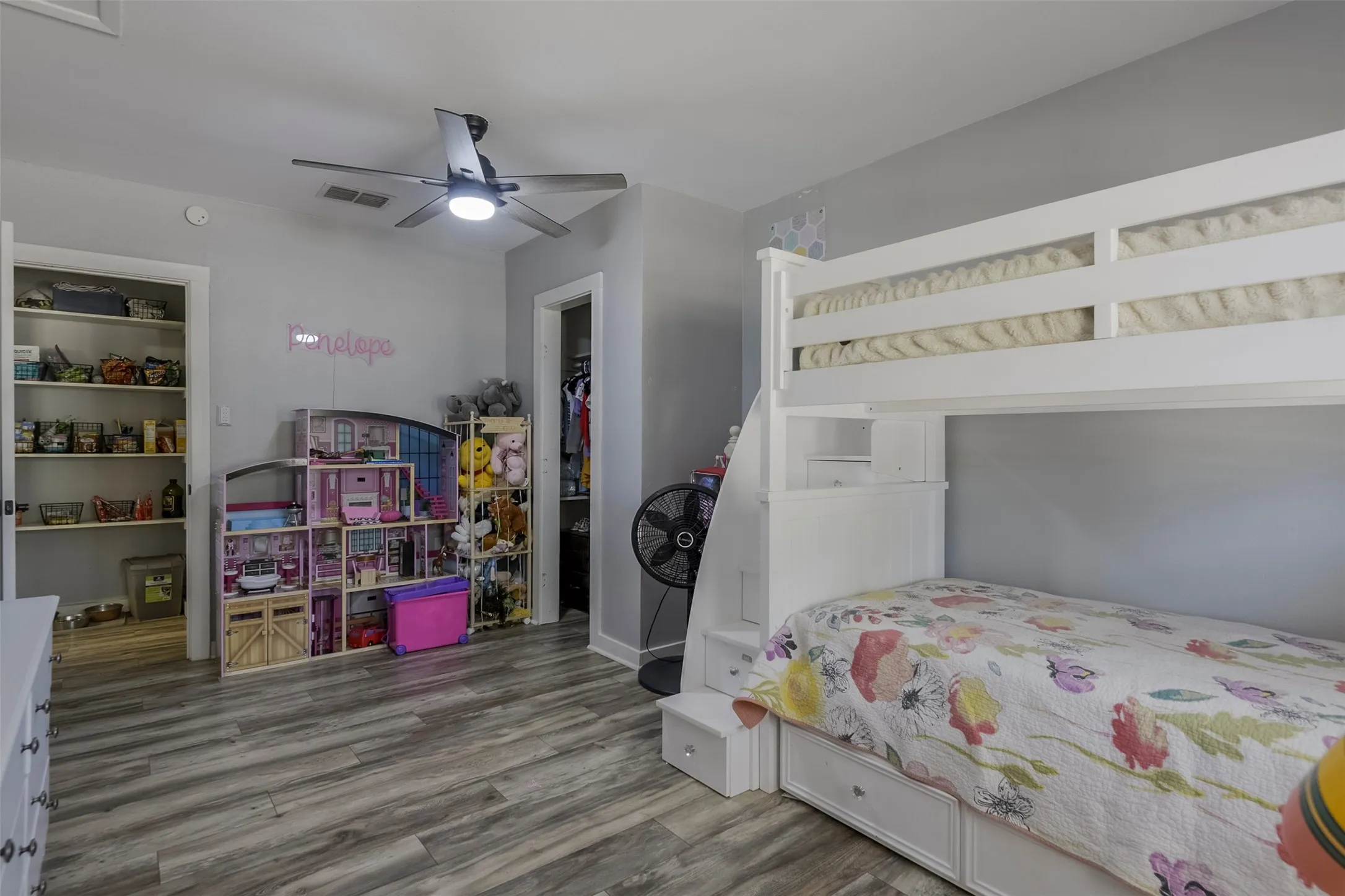 Light gray walls with wood-finish flooring, featuring a ceiling fan with integrated lighting, and two open closet entries