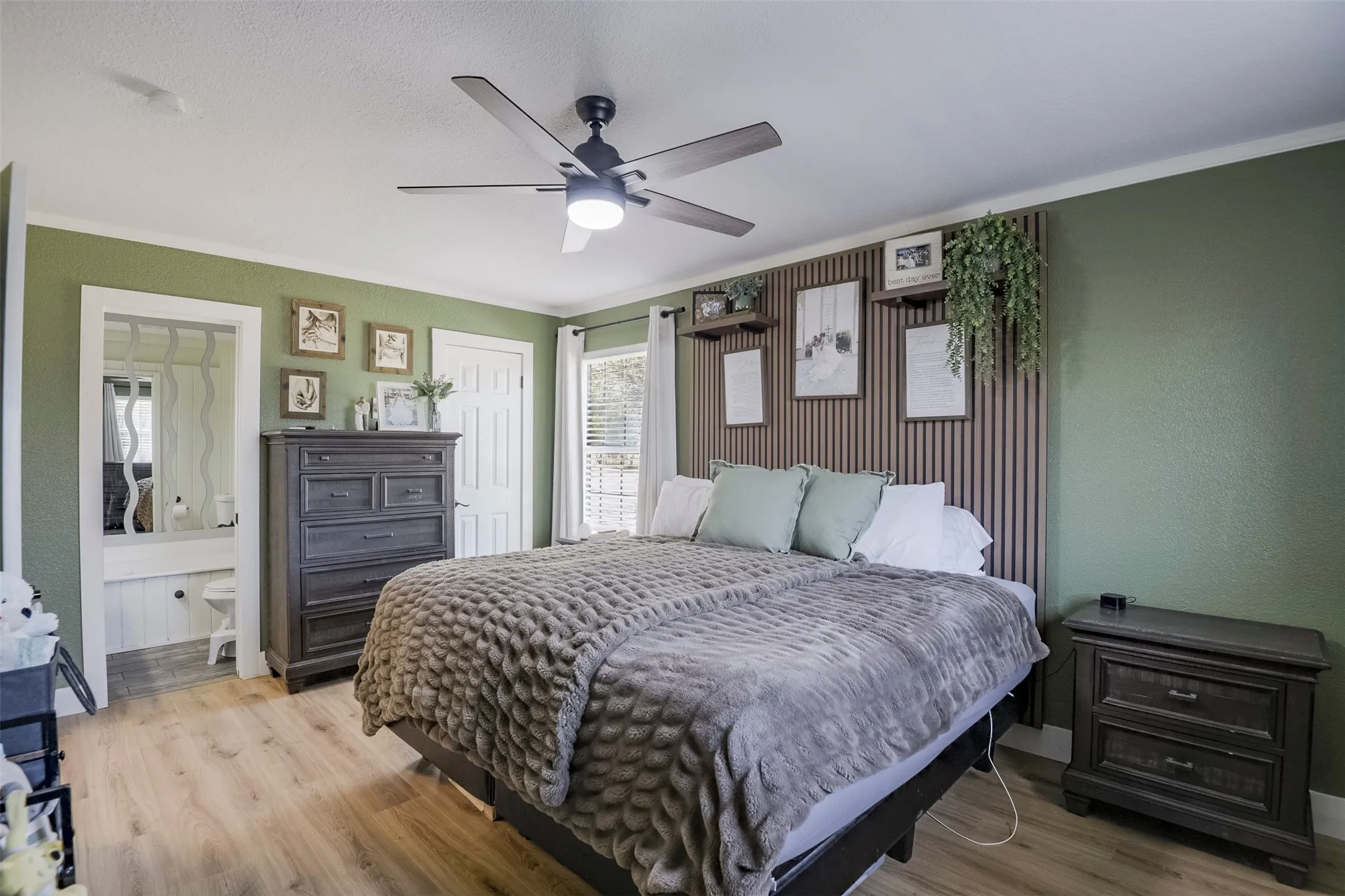 Wood-finish flooring with a ceiling fan, accent wall with shelving, and built-in vanity area