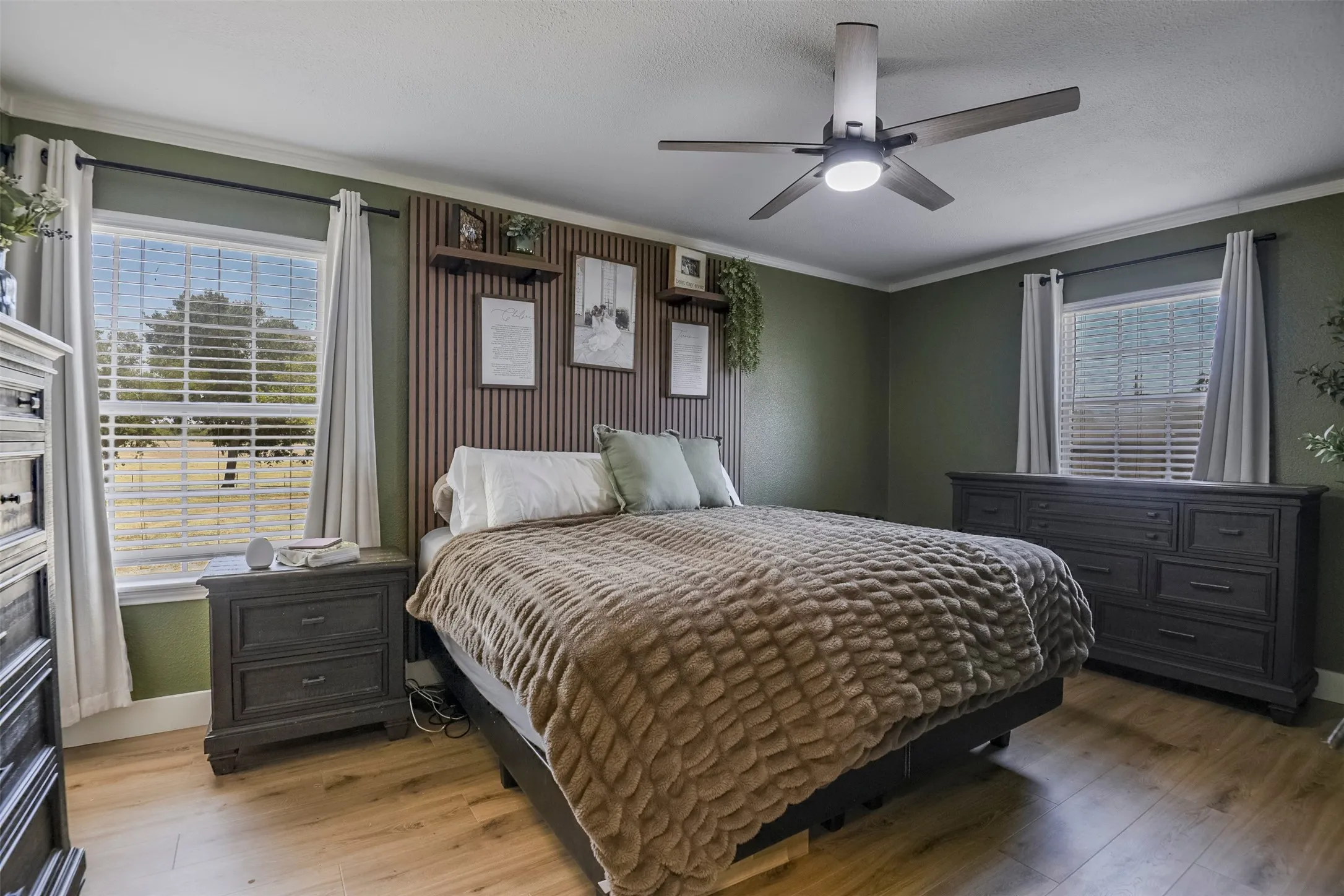 Wood-finish flooring, accent wall with vertical wood paneling, contemporary ceiling fan, and crown molding