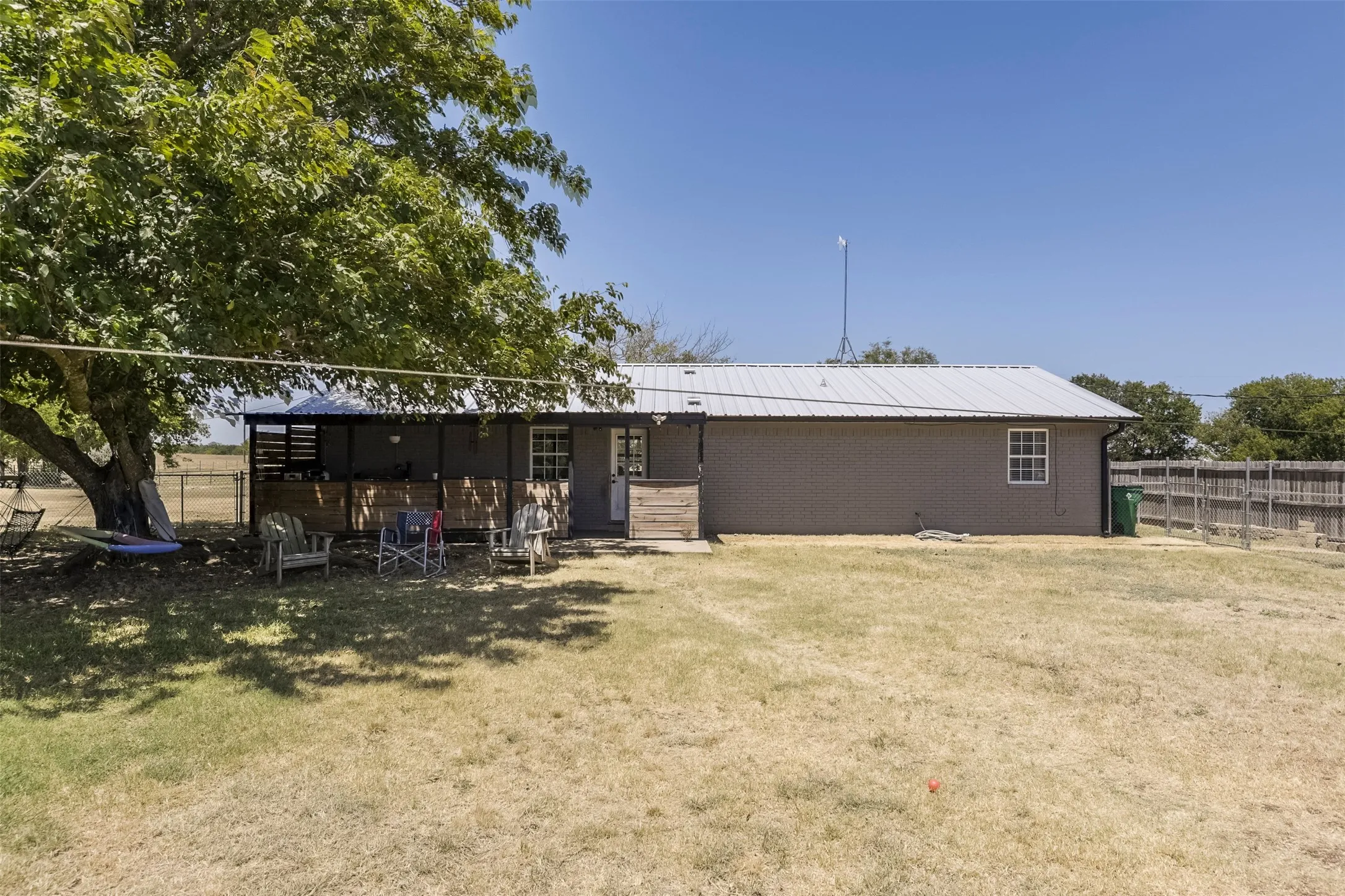 Expansive yard featuring a large mature tree, wood-slat privacy fence, covered patio, and metal roof