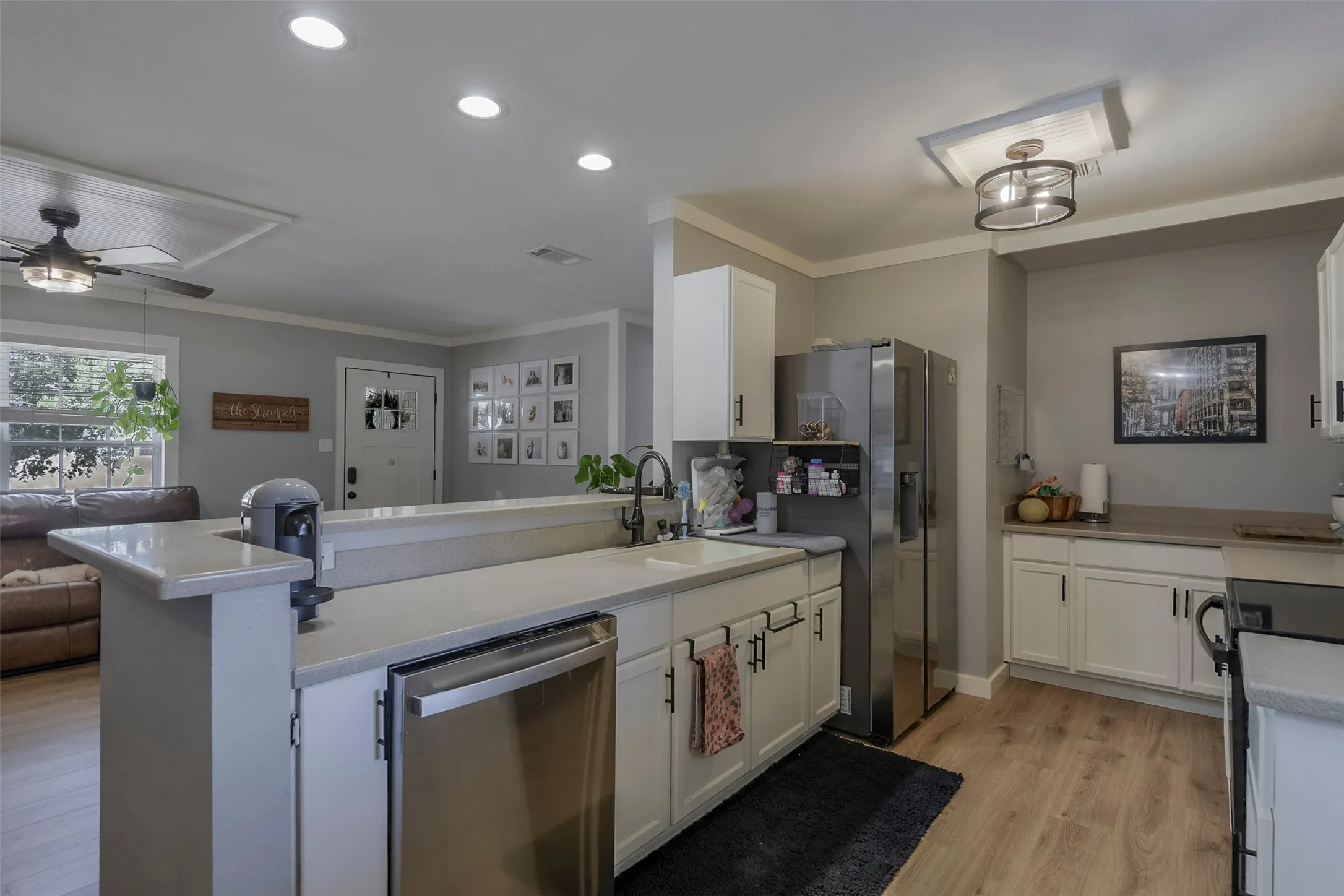 Kitchen featuring wood-finish flooring, white cabinetry, stainless steel appliances, and light-toned countertops