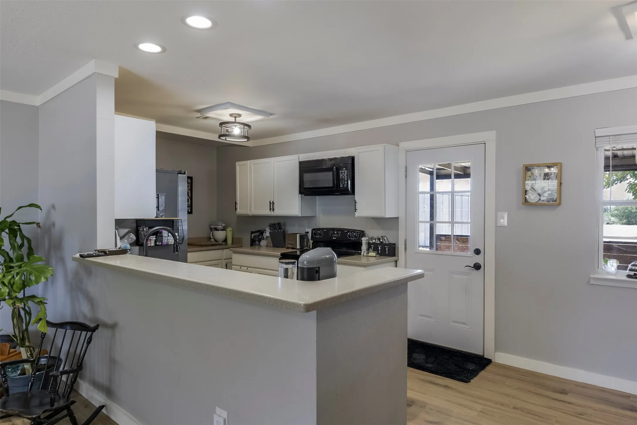 Kitchen featuring white cabinetry, black appliances, light-toned countertops, and wood-finish flooring