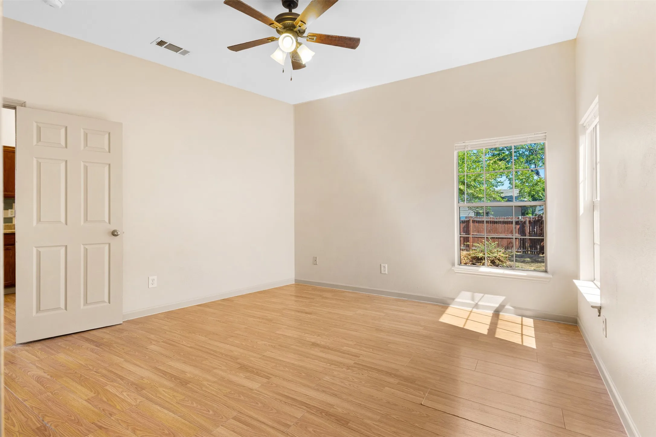 Wood-finish flooring with a multi-pane window, ceiling fan, and six-panel interior door