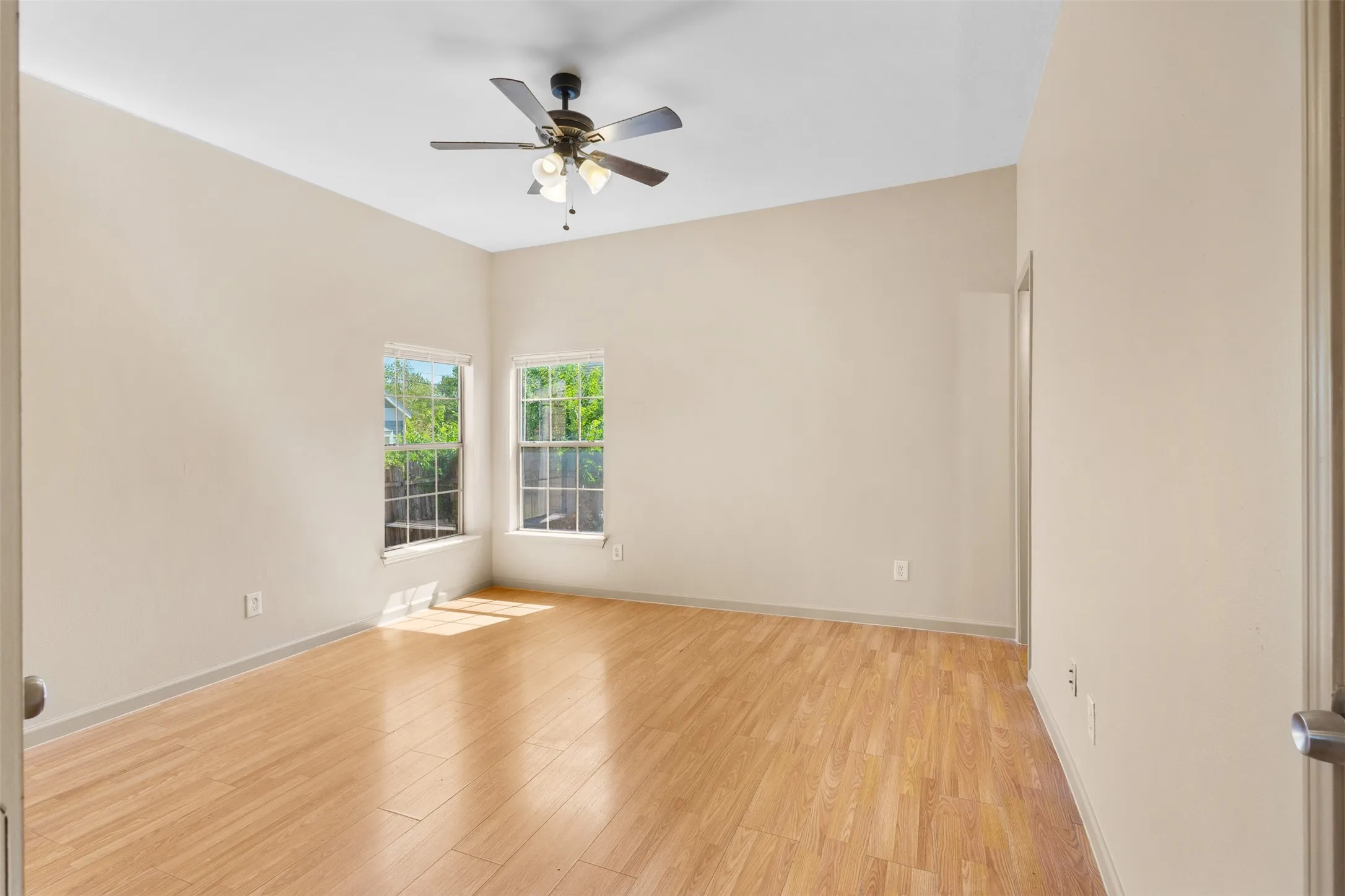 Vaulted ceiling, ceiling fan with integrated lighting, wood-finish flooring, two windows, neutral wall tones