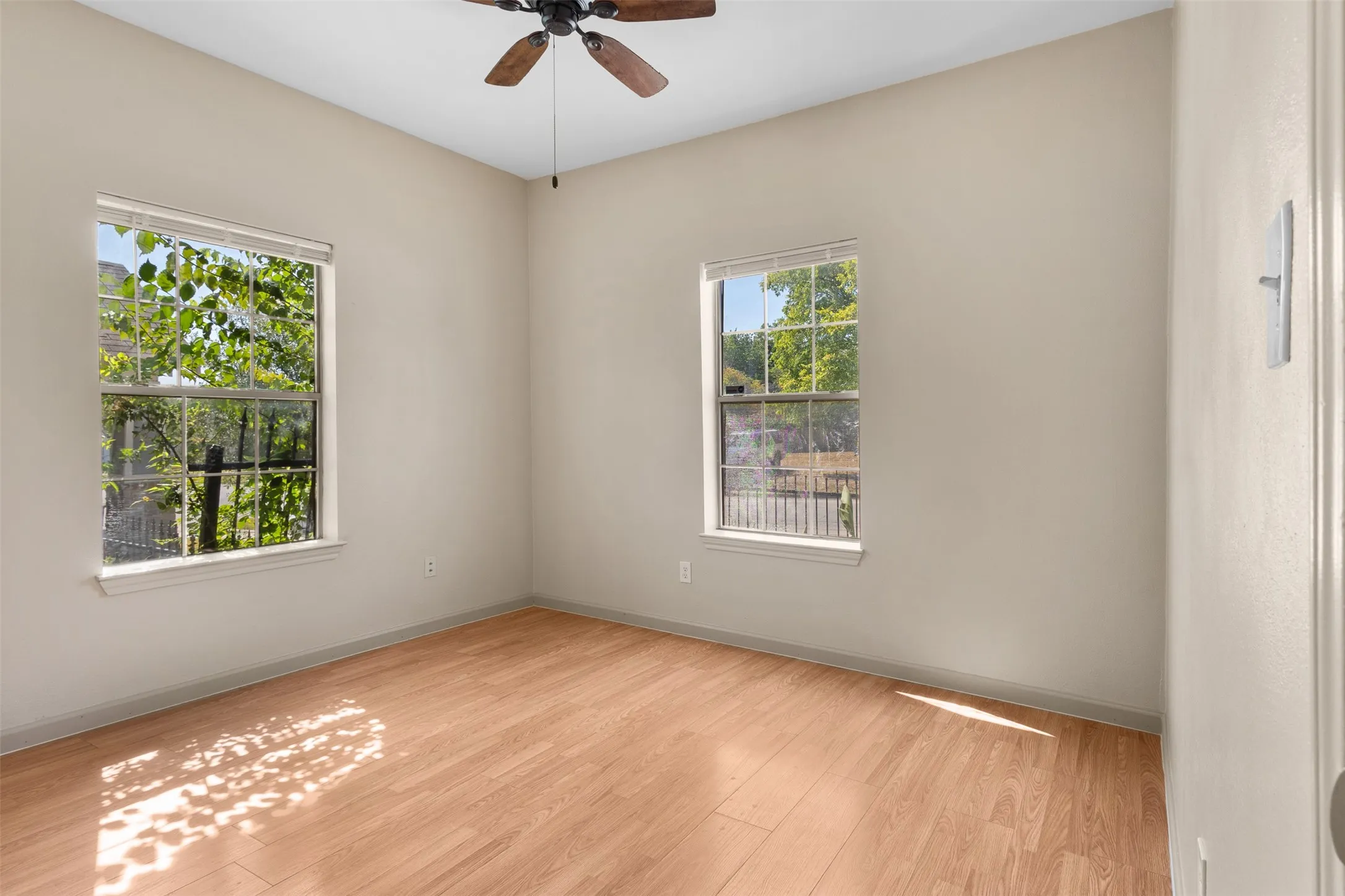 Wood-finish flooring with light-toned walls, dual windows, and a ceiling fan with integrated lighting