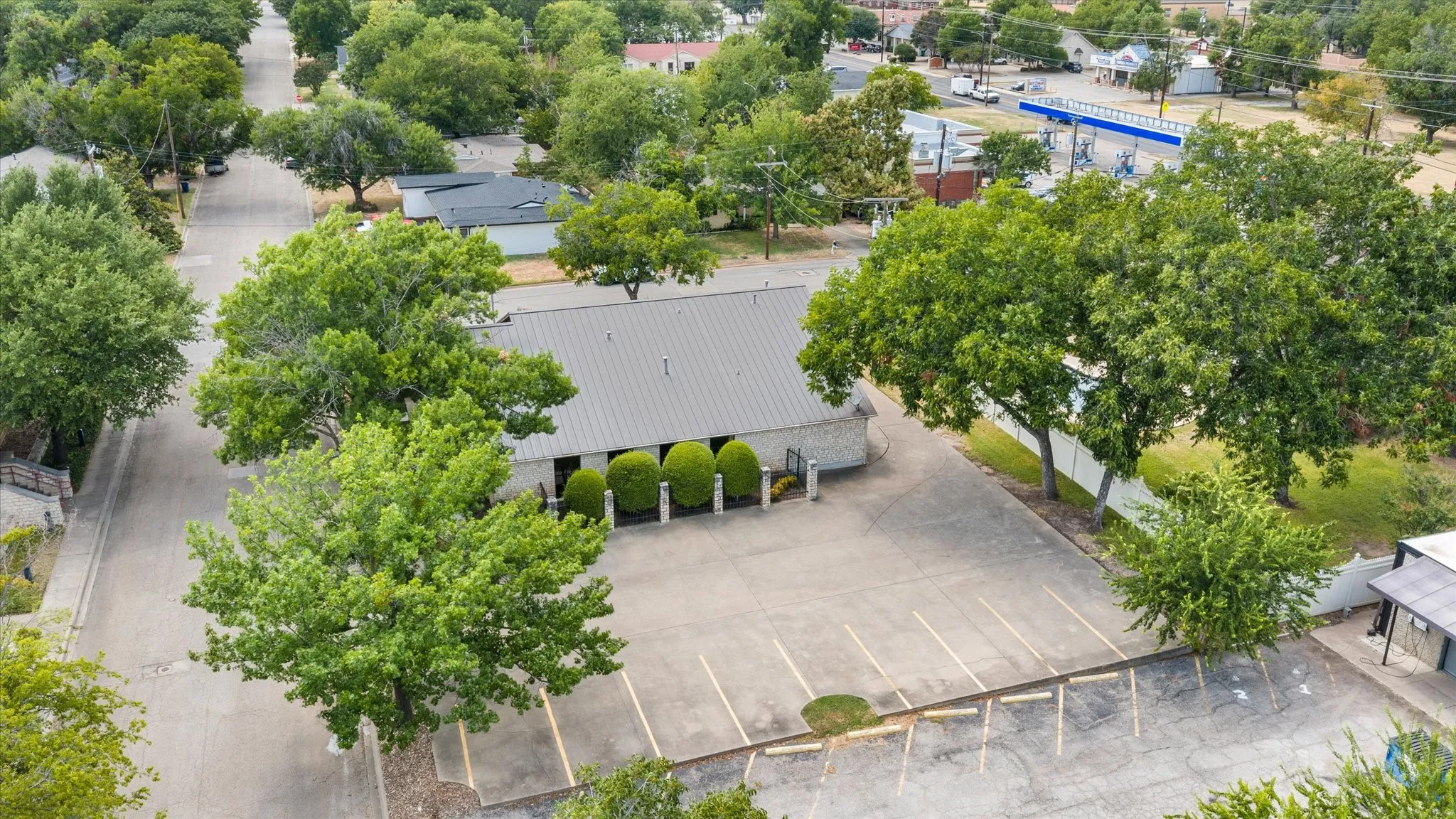 Paved parking lot with marked spaces, mature trees, and a metal-roofed building
