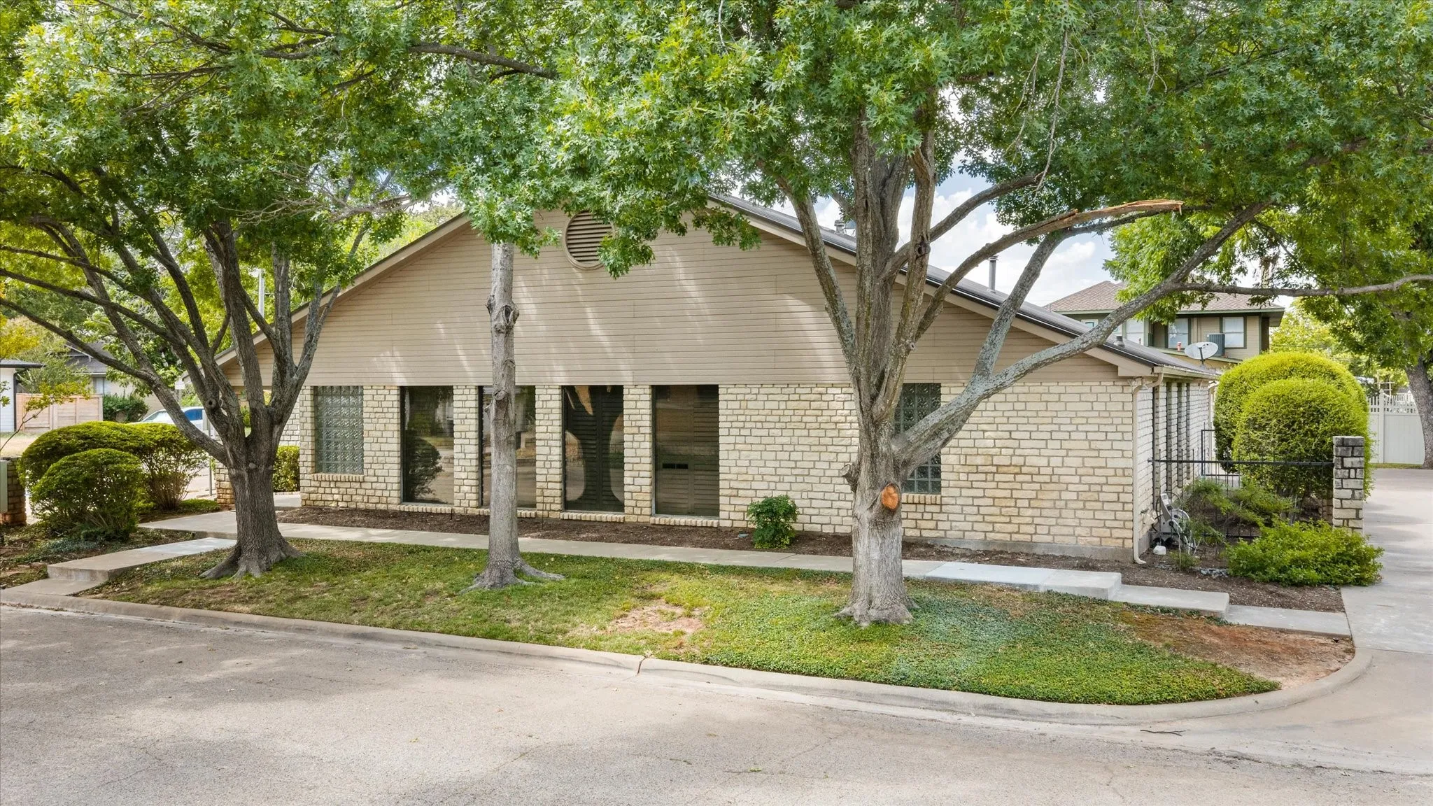 Single-story structure with a brick and siding exterior, large windows, and mature trees