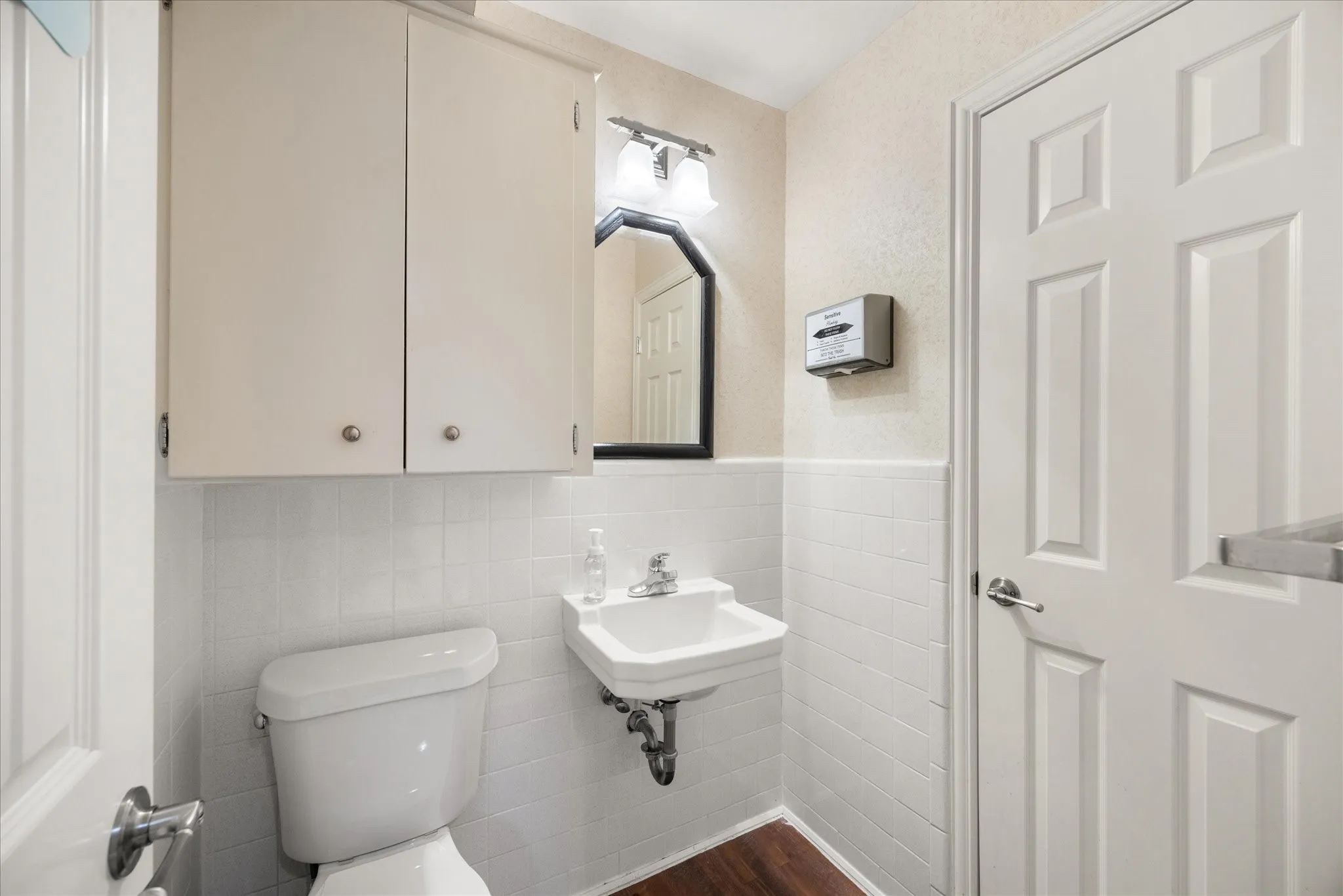 White wall-mounted cabinetry, wall-mounted sink, and a rectangular mirror with wall sconce lighting