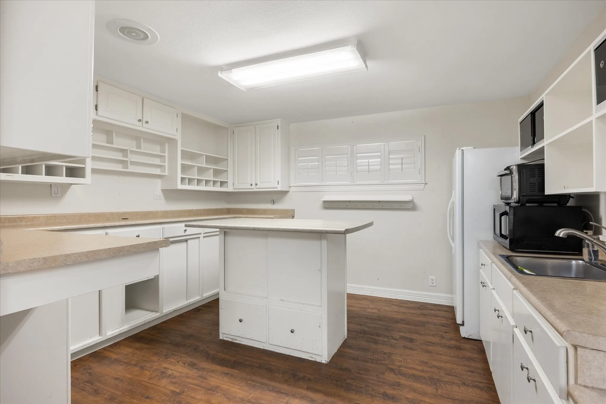 Functional kitchen featuring extensive white cabinetry, wood-finish flooring, a central island, and abundant counter space