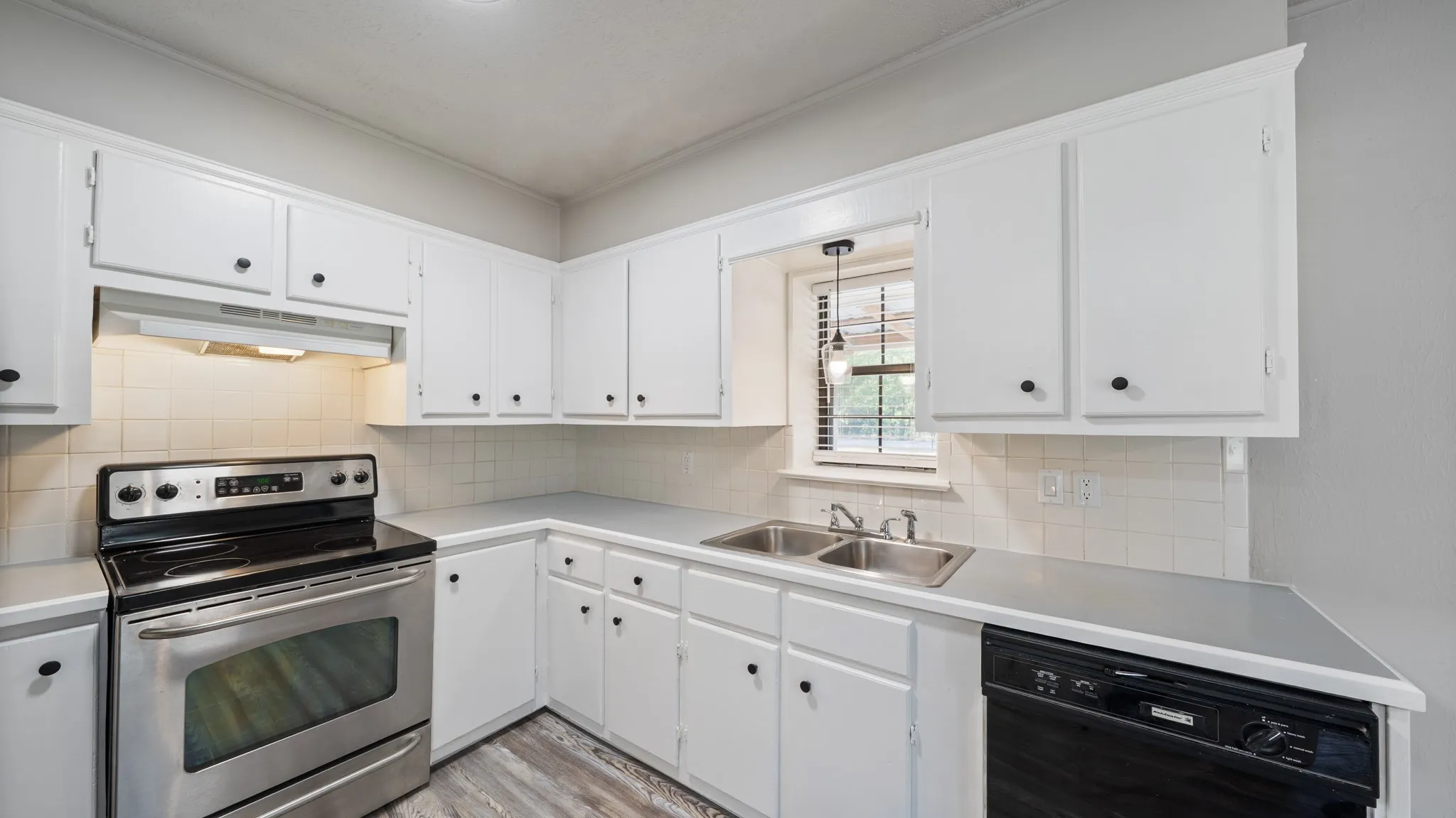 White cabinetry with black hardware, stainless steel electric range, dual basin sink, white tile backsplash, and wood-finish flooring