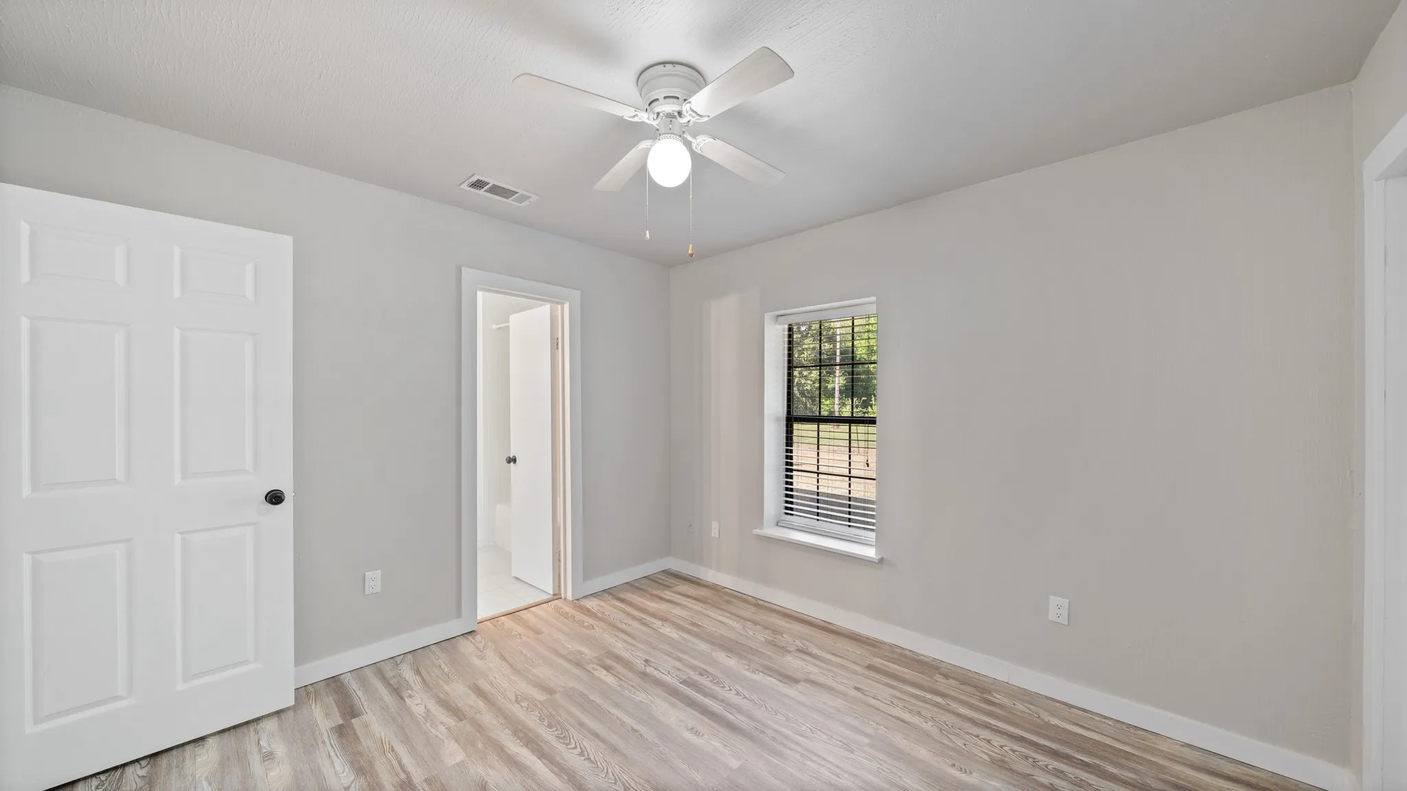 Wood-finish flooring, light gray wall finishes, white ceiling fan, and a window with blinds