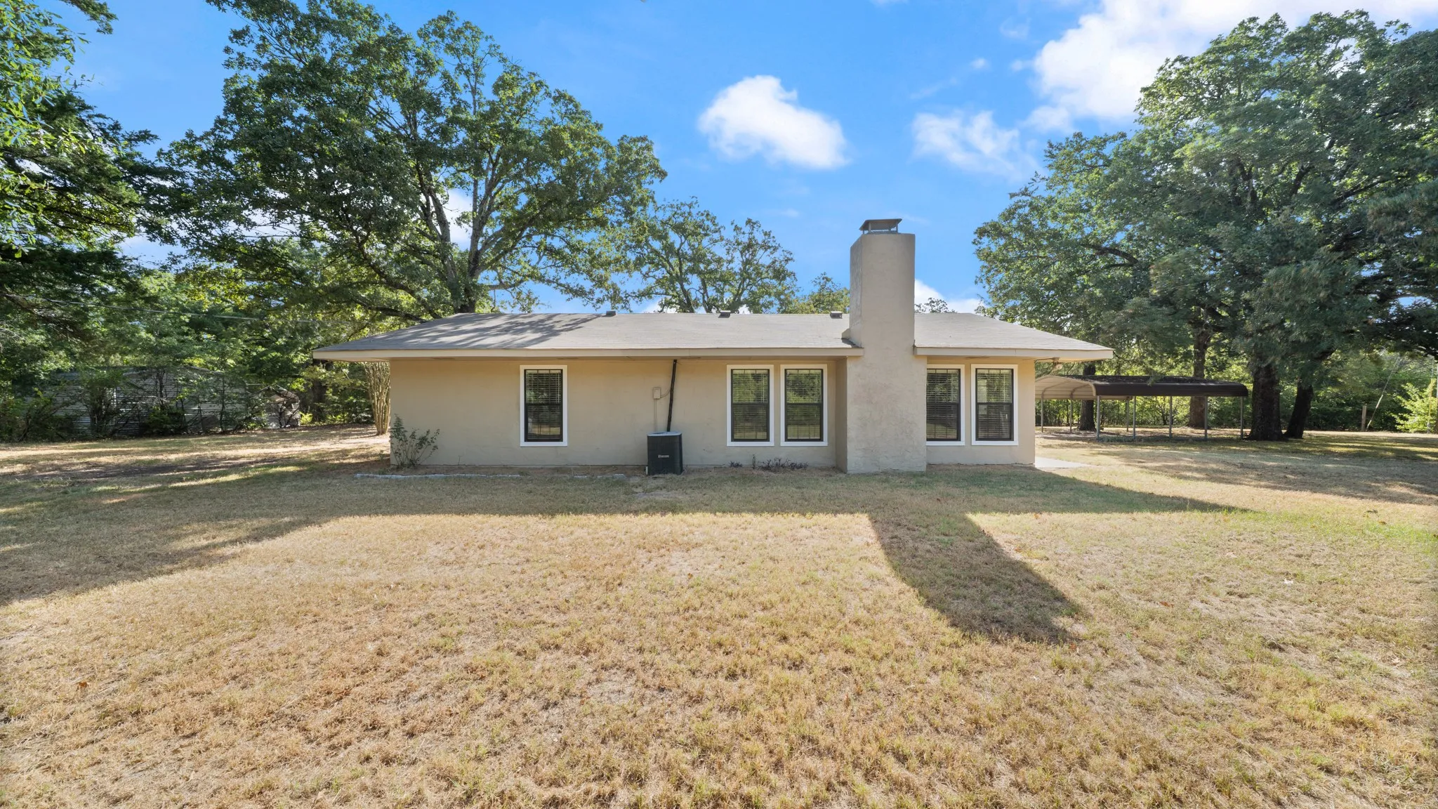 back featuring a stucco exterior, multiple windows with dark framing, a prominent chimney, and a covered outdoor area