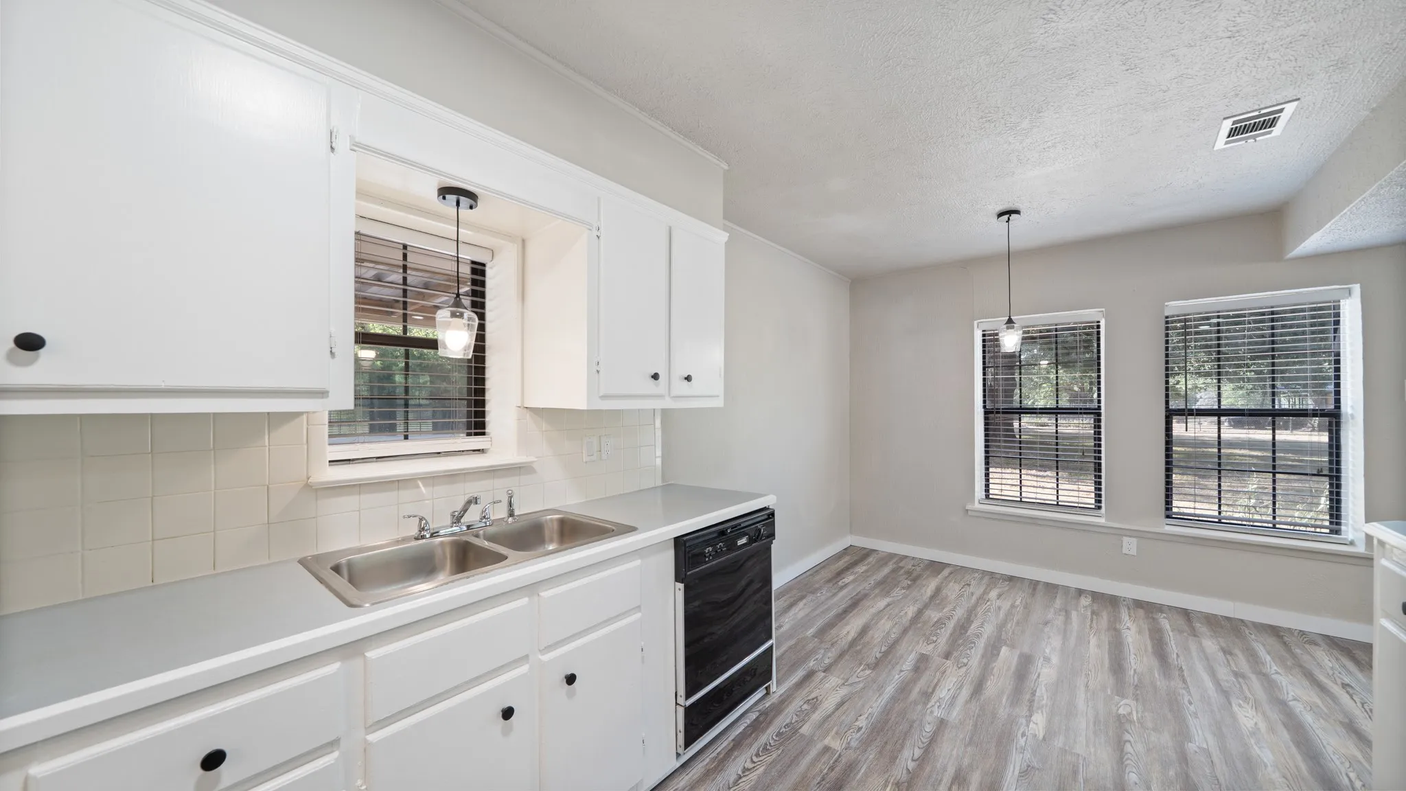Kitchen featuring white cabinetry, a dual basin sink, white subway tile backsplash, and wood-finish flooring