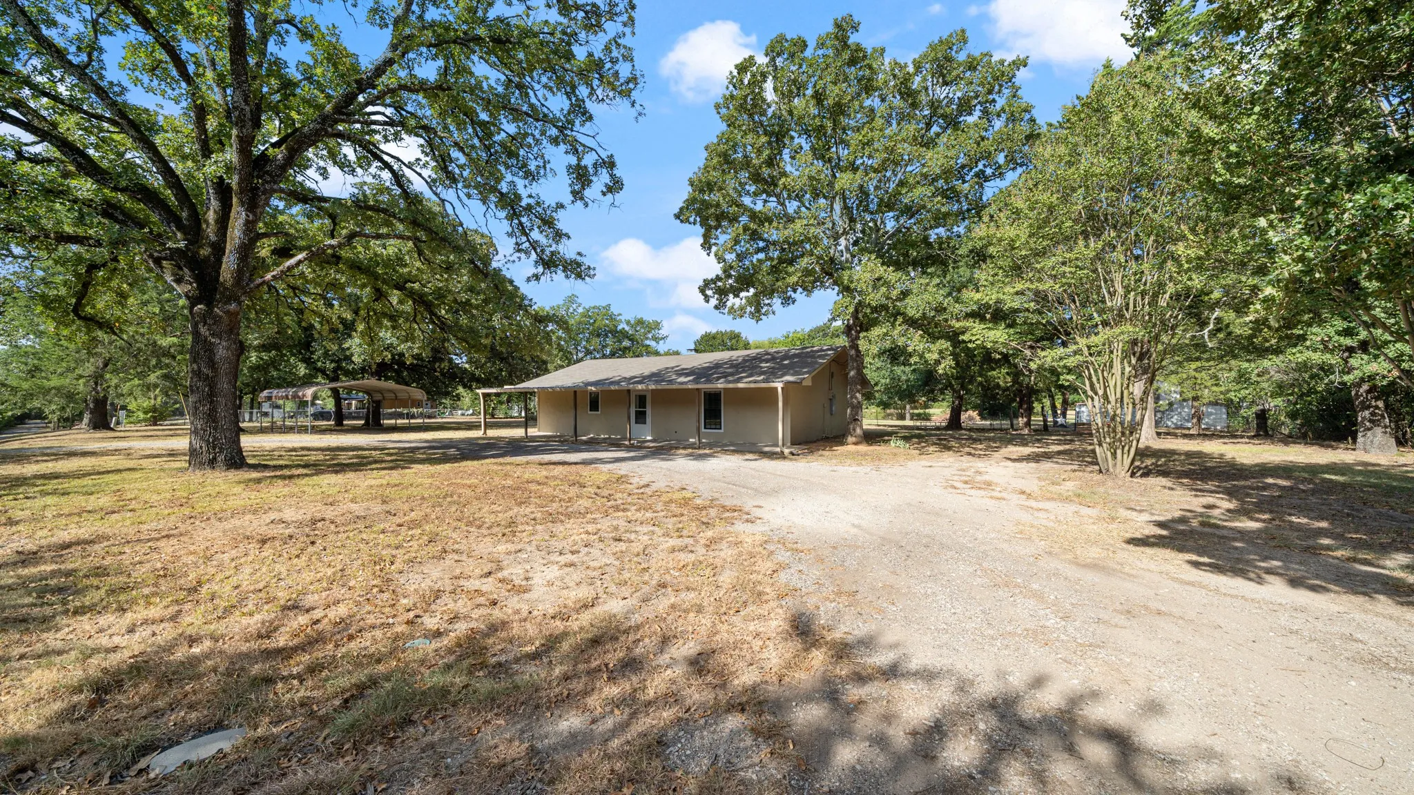 Front with a covered front porch, gravel driveway, and mature trees