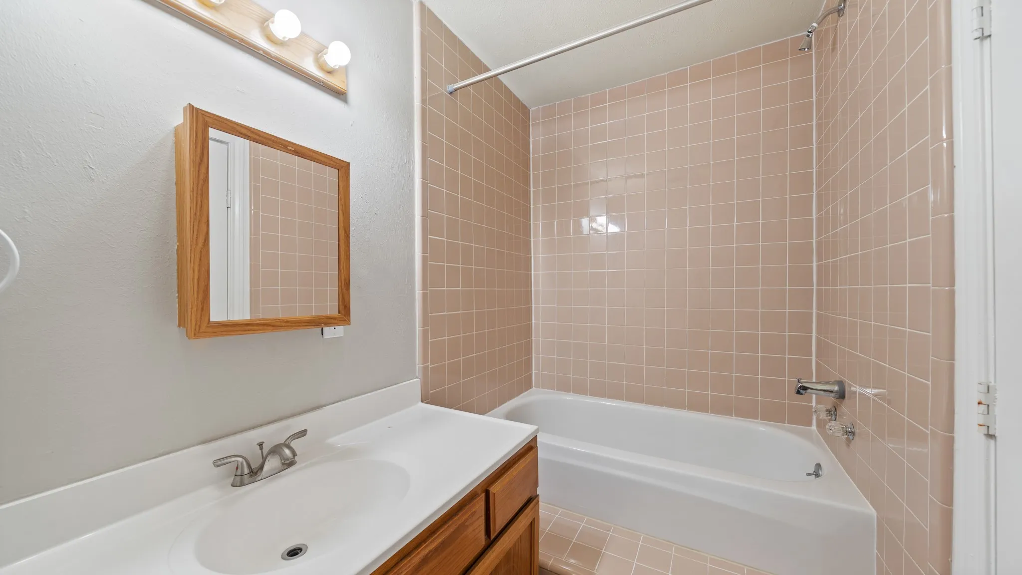 Bathroom featuring a built-in tub, extensive wall tiling, vanity with an integrated sink, and a wall-mounted mirrored cabinet