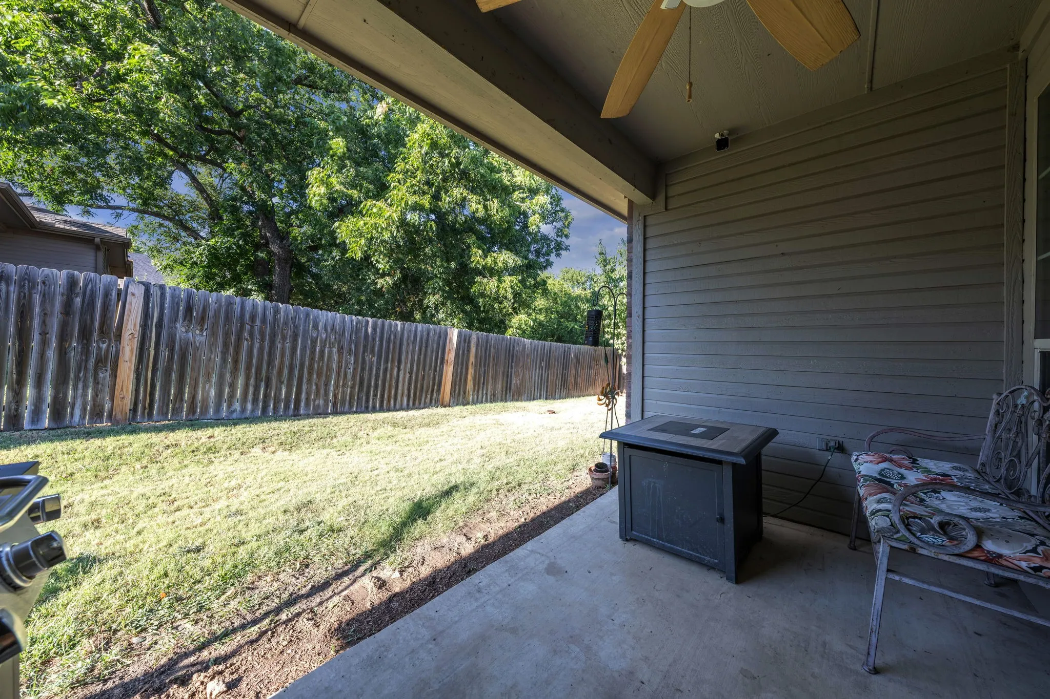 Covered concrete patio with ceiling fan, wood privacy fence, and expansive lawn area