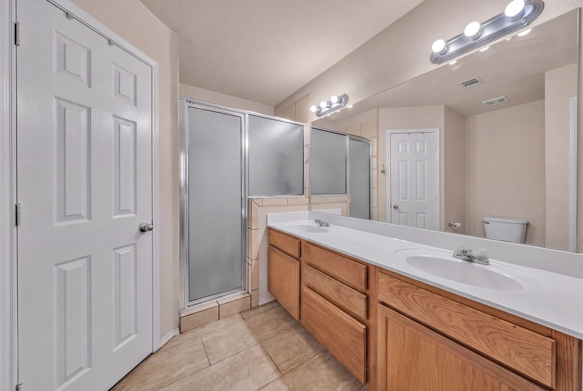 Dual vanity with white countertops, light wood-finish cabinetry, and an expansive wall-mounted mirror