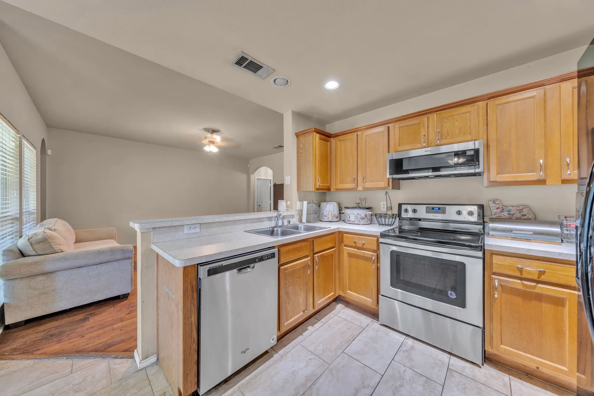Kitchen featuring wood cabinetry, stainless steel appliances, a double basin sink, and tile flooring